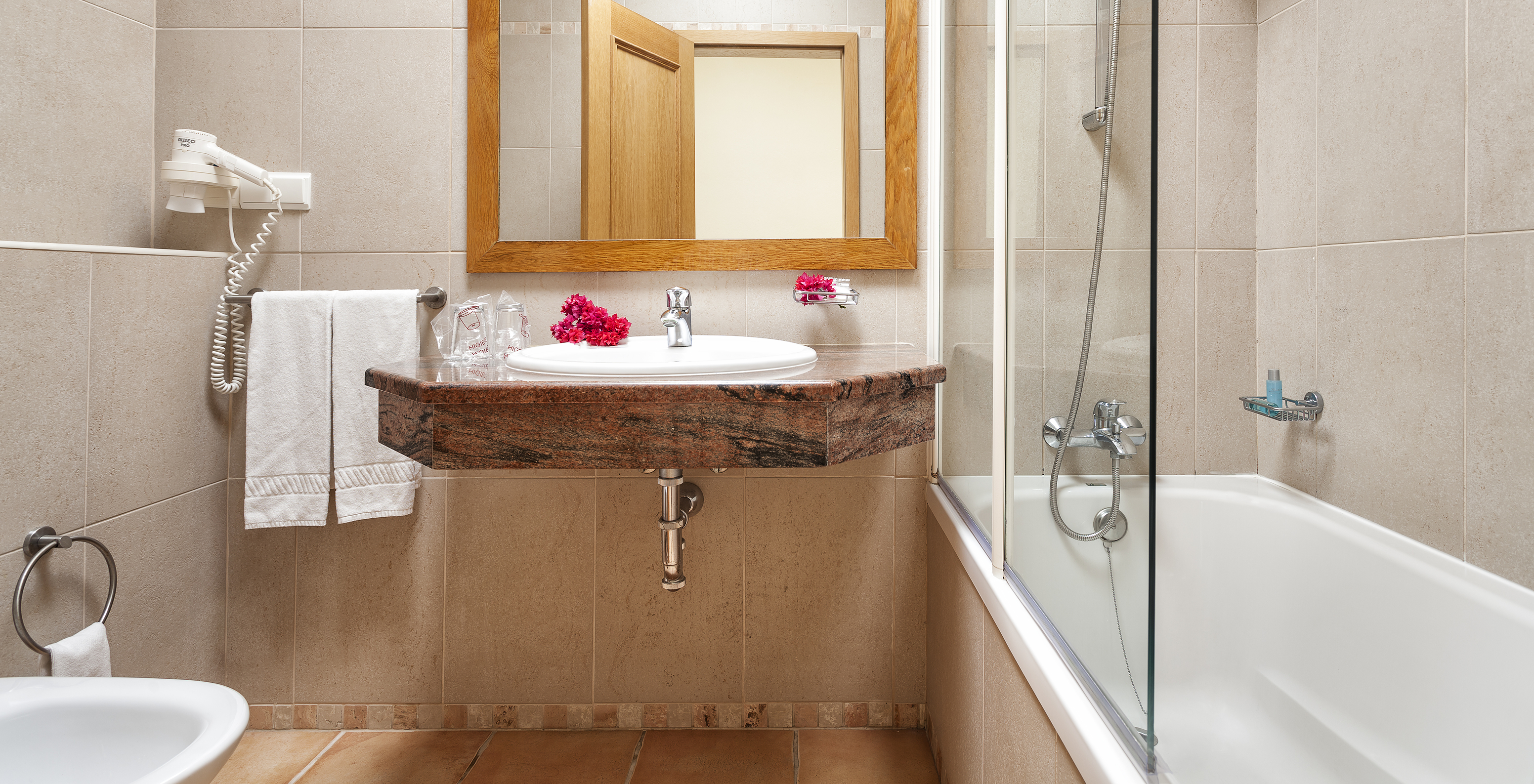 L'Appartement T1 - Terra du Pestana Palm Gardens a une baignoire avec douche, un lavabo avec fleurs et un miroir