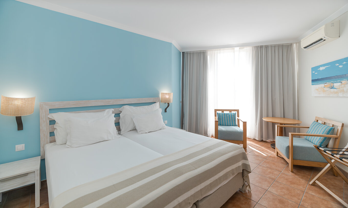Le Deluxe Vue Mer du Pestana Viking a deux lits, table de chevet, deux fauteuils et climatisation