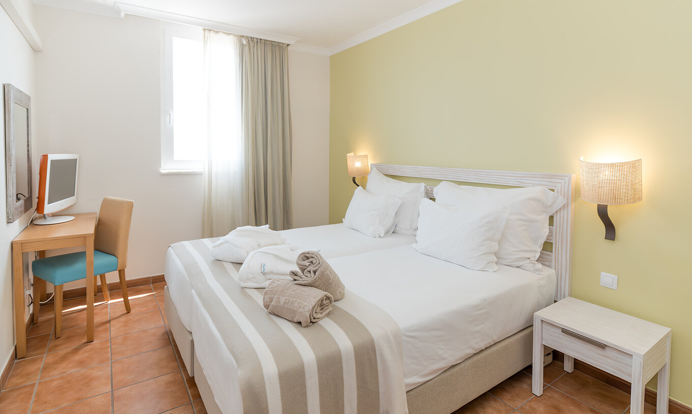 La Suite Supérieure Vue Mer du Pestana Viking comprend deux lits simples, table de chevet, télévision et miroir