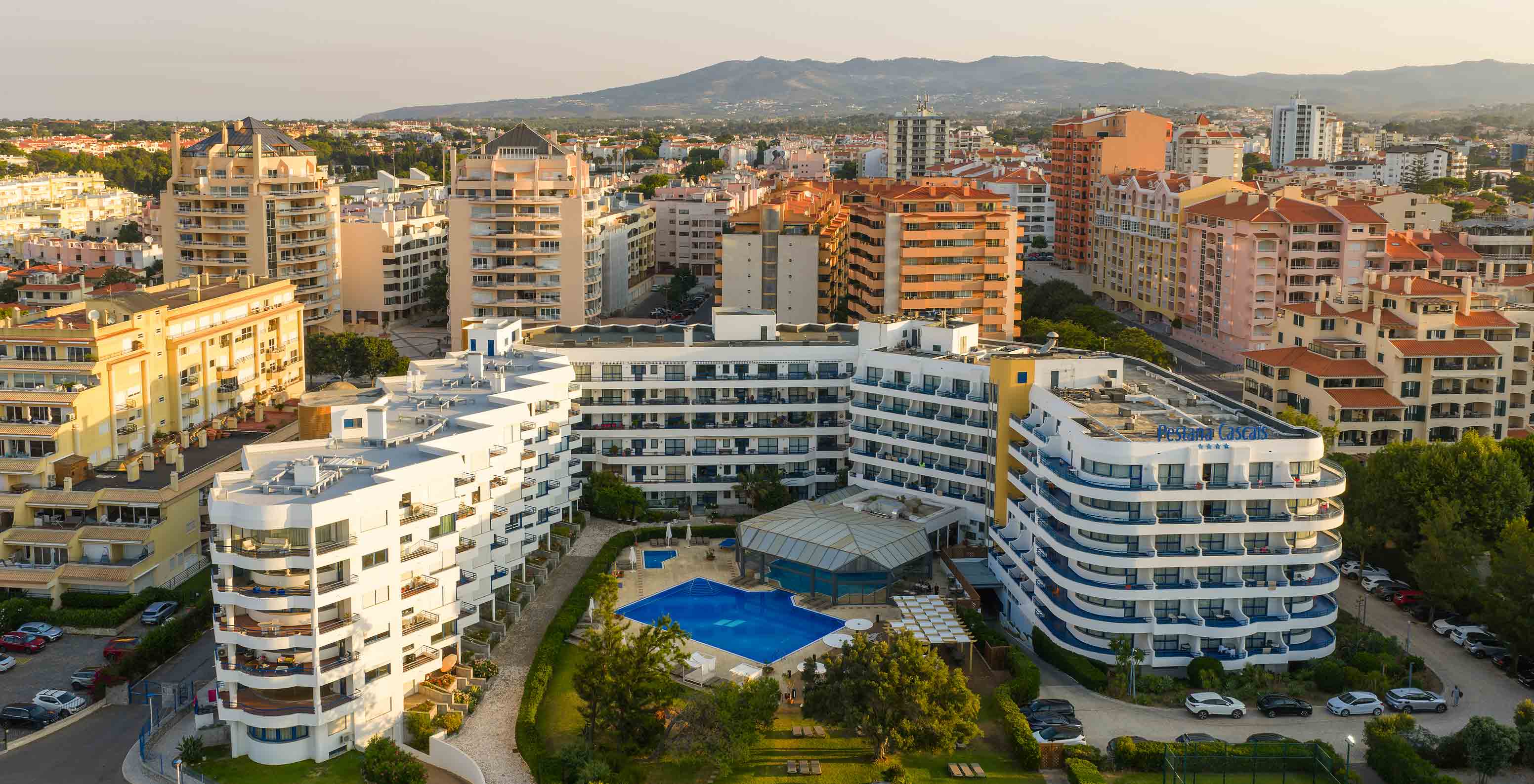 Vue aérienne de l'hôtel avec les balcons, les piscines et le jardin, et la ville derrière avec la montagne au fond