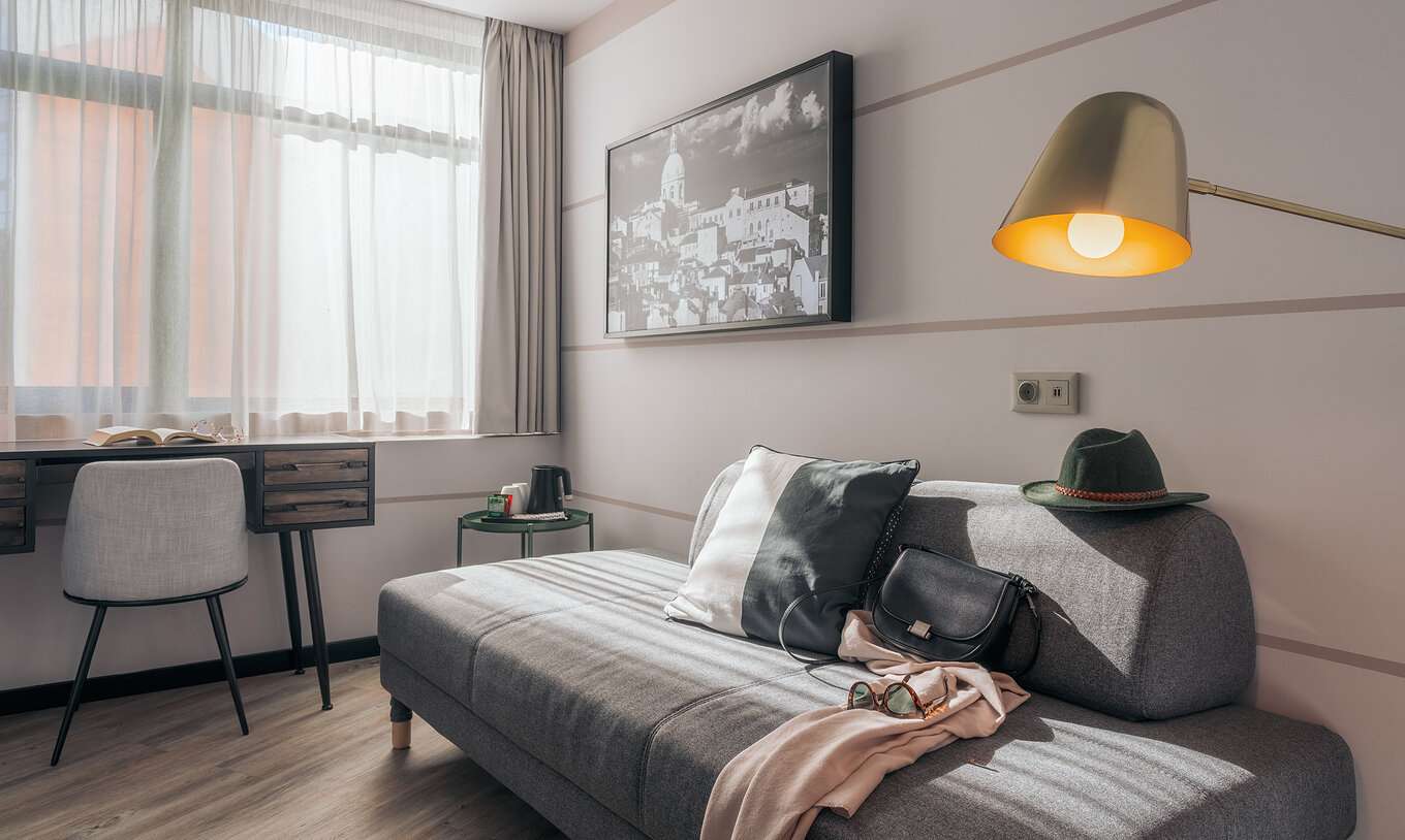 Le Double Supérieur du Pestana Lisboa Vintage a un canapé gris une bureau avec chaise une table d'appoint et un tableau