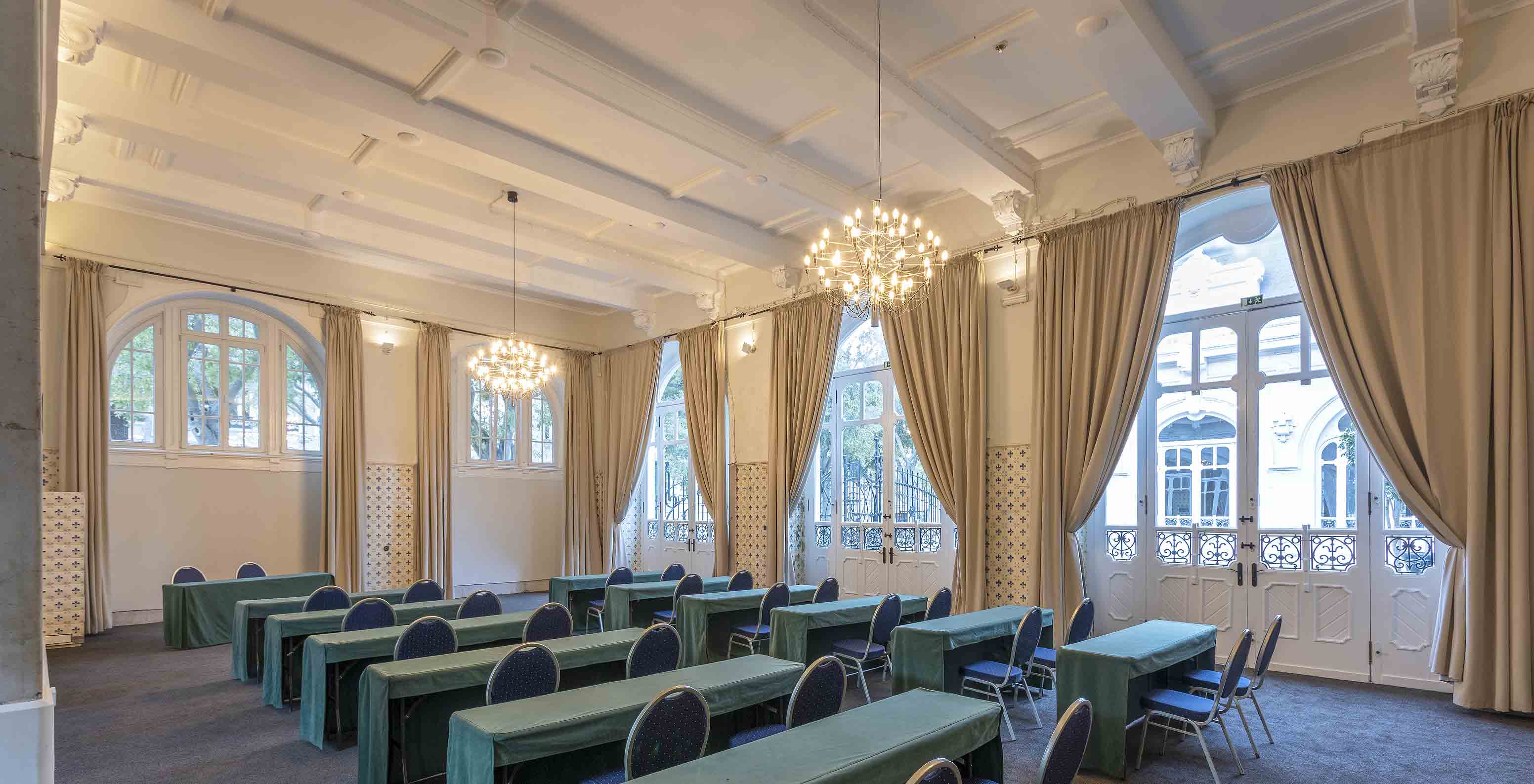 Le Pestana Palace dispose d'une salle de réunion avec de longues tables vertes, des chaises bleues et plusieurs fenêtres