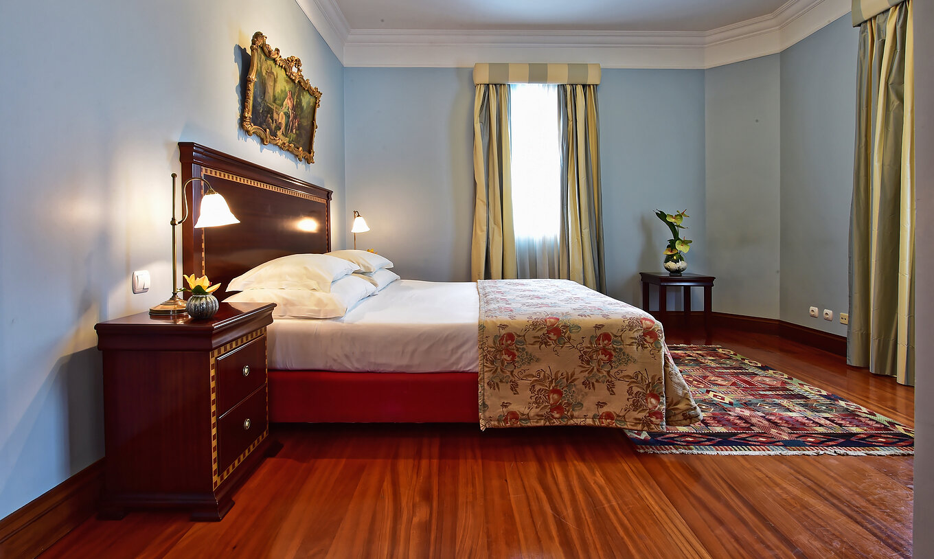 La Suite Miramar du Pestana Miramar a un lit double avec une couverture florale et une table de chevet en bois foncé