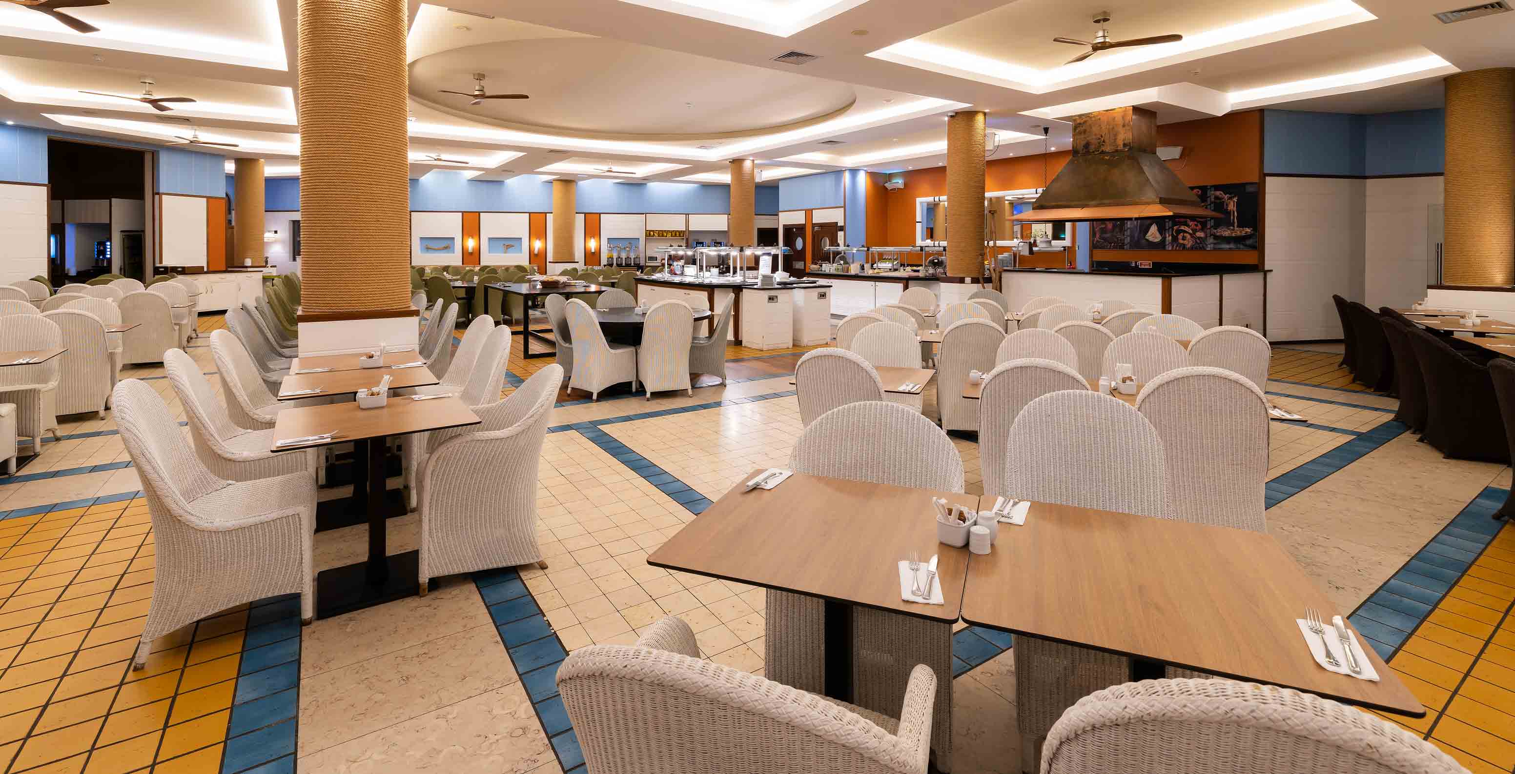 Grand espace du restaurant Marés du Pestana Porto Santo avec des détails bleus et jaunes et des chaises blanches