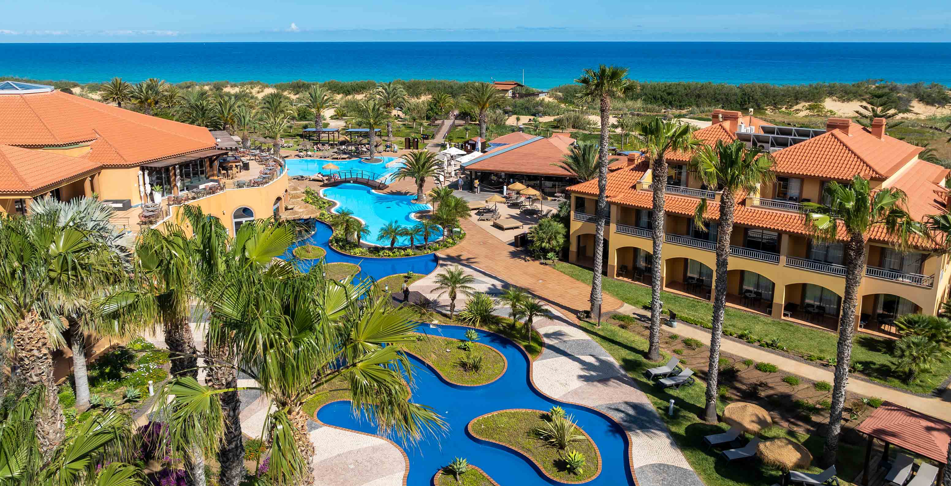 Piscine extérieure bleue du Pestana Porto Santo All Inclusive, entourée de palmiers, de villas et de jardins