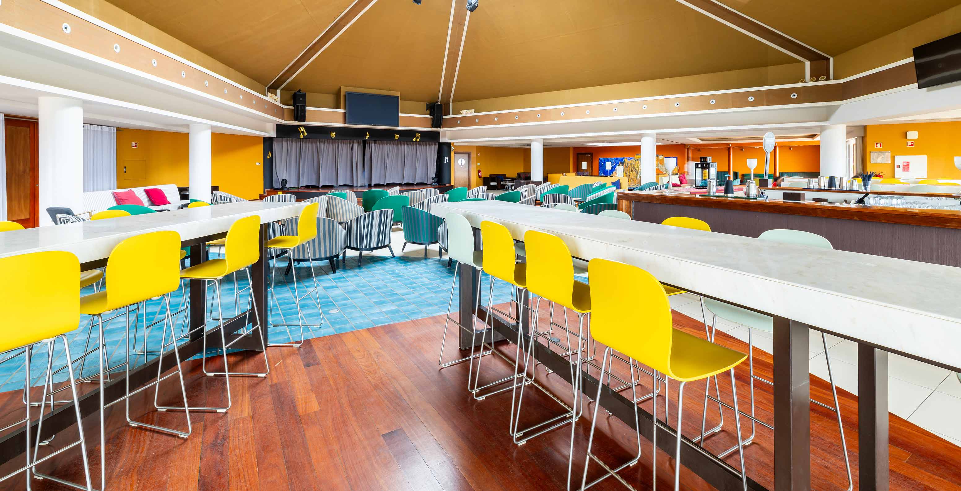 Le bar Sunset du Resort 5 étoiles à Porto Santo a des tables hautes avec des tabourets jaunes et blancs.