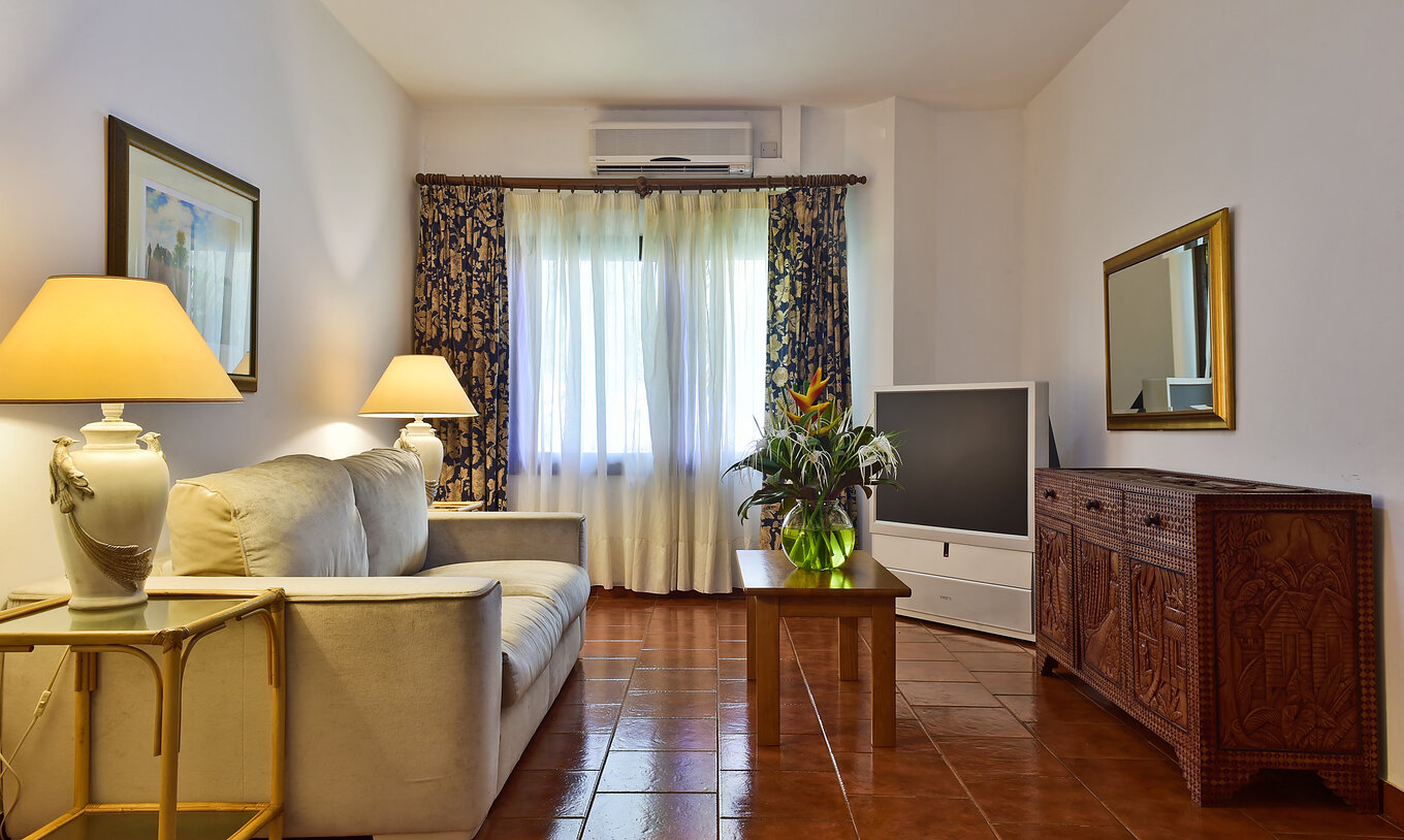 La Suite du Pestana Miramar São Tomé a un salon avec canapé, télévision et une table avec un vase de fleurs