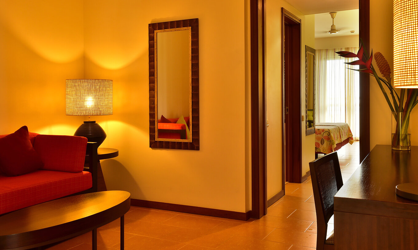 La Junior Suite du Pestana São Tomé a un salon avec canapé rouge et une table basse, et un bureau avec fleurs