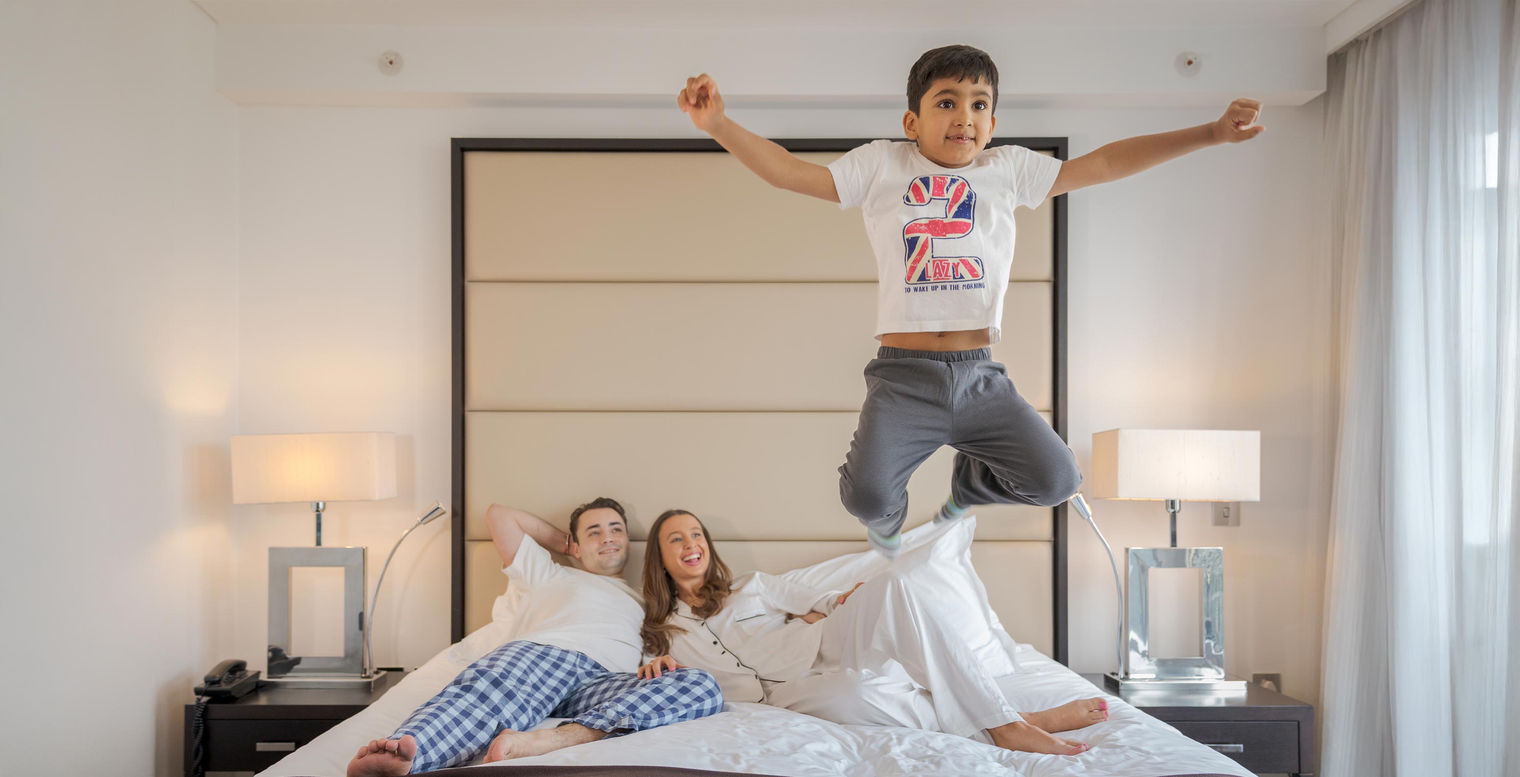 Le Deluxe Family du Pestana Chelsea Bridge a un lit double avec famille allongée et enfant qui saute