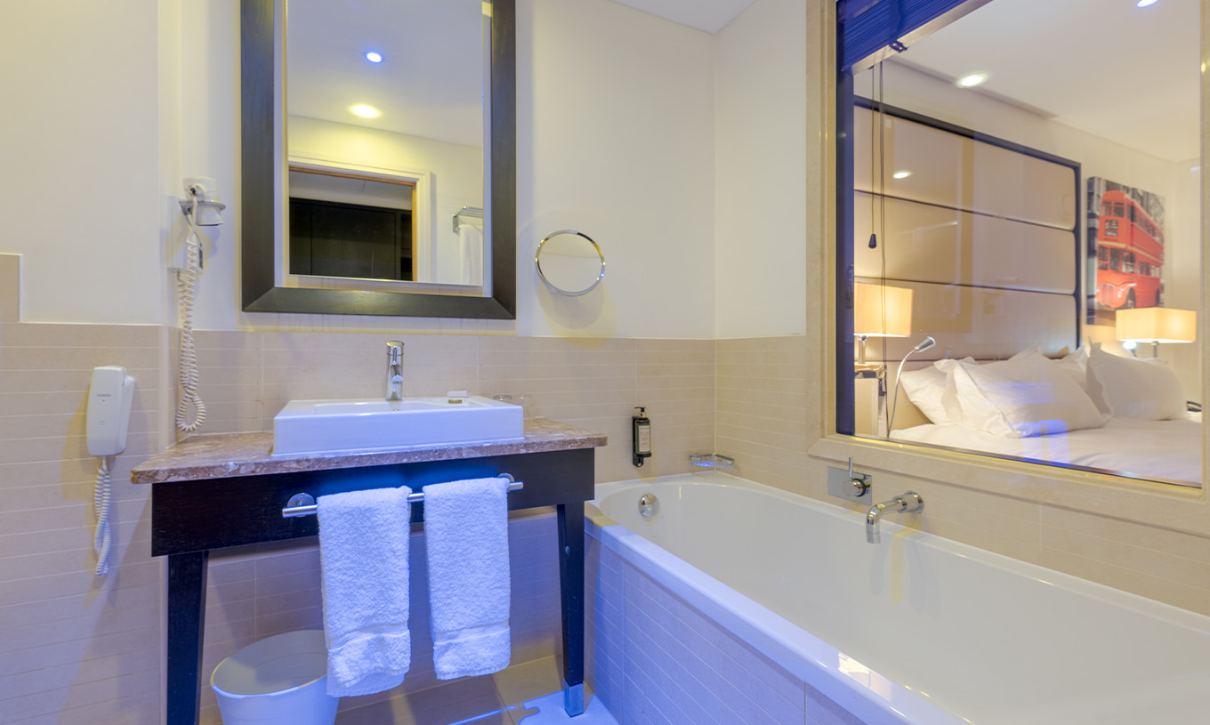 Le Twin Deluxe du Pestana Chelsea Bridge a une salle de bains avec baignoire, vitre pour la chambre, lavabo et sèche-cheveux