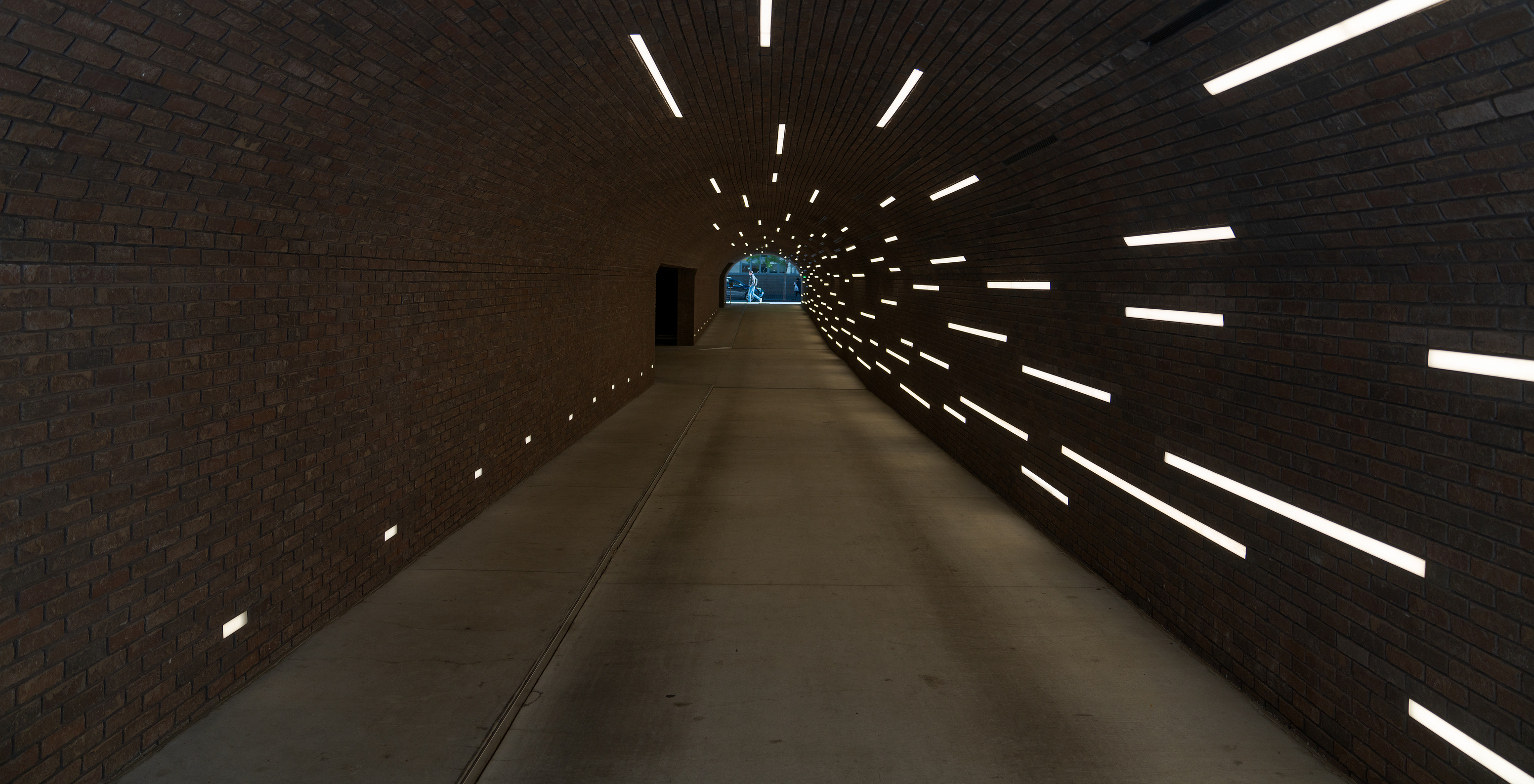 Vue de l'intérieur d'un tunnel avec un sol en béton et des murs en briques, éclairé par des lignes de lumière fluorescente