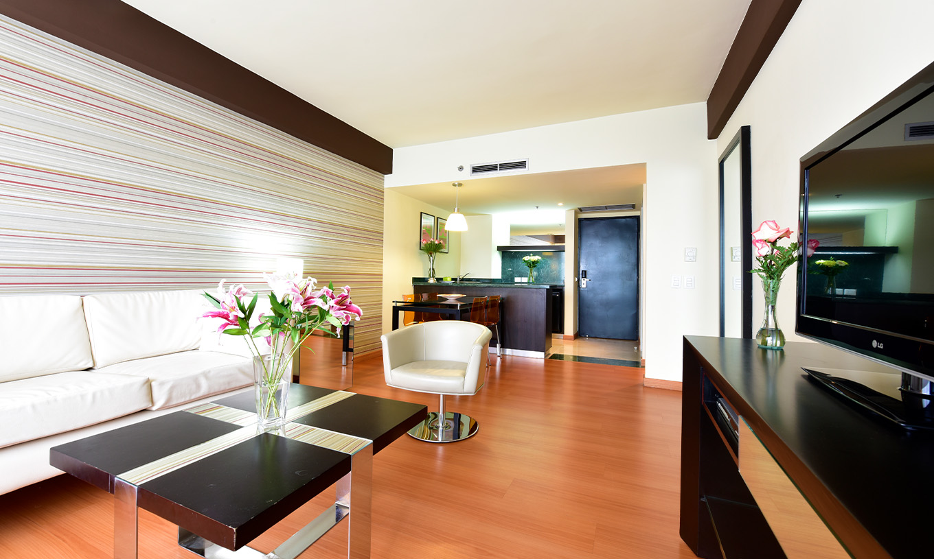 La King Junior Suite du Pestana Caracas a une salle avec un canapé blanc confortable, une table d'appoint et une télévision