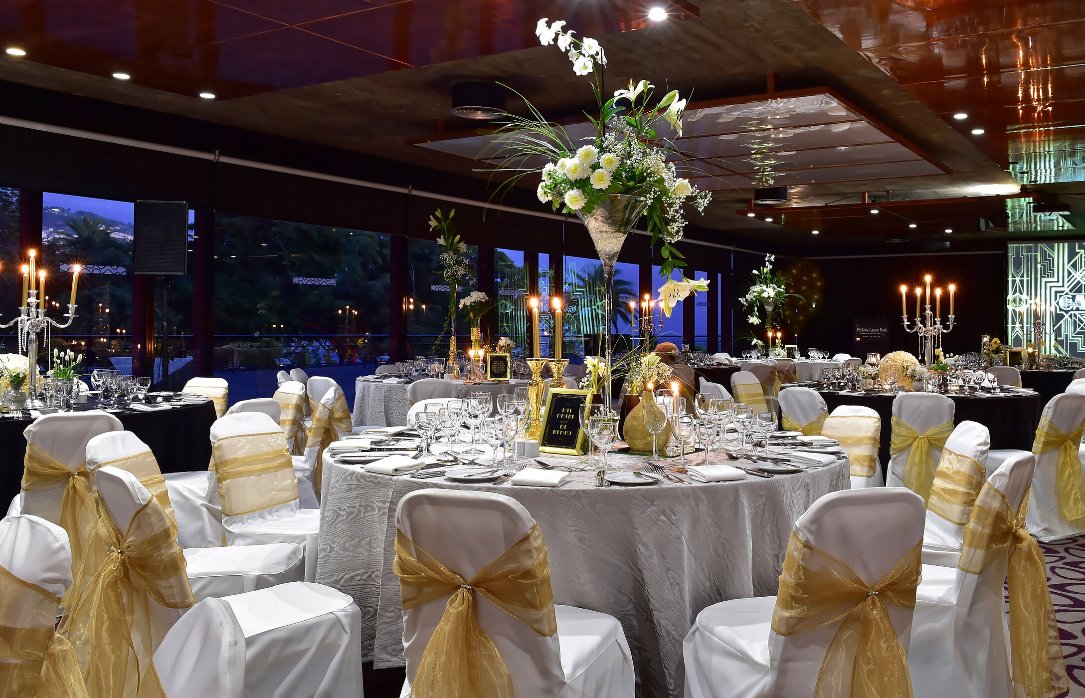 Mariage dans une salle moderne avec tables rondes, arrangements floraux hauts et éclairage doux et élégant