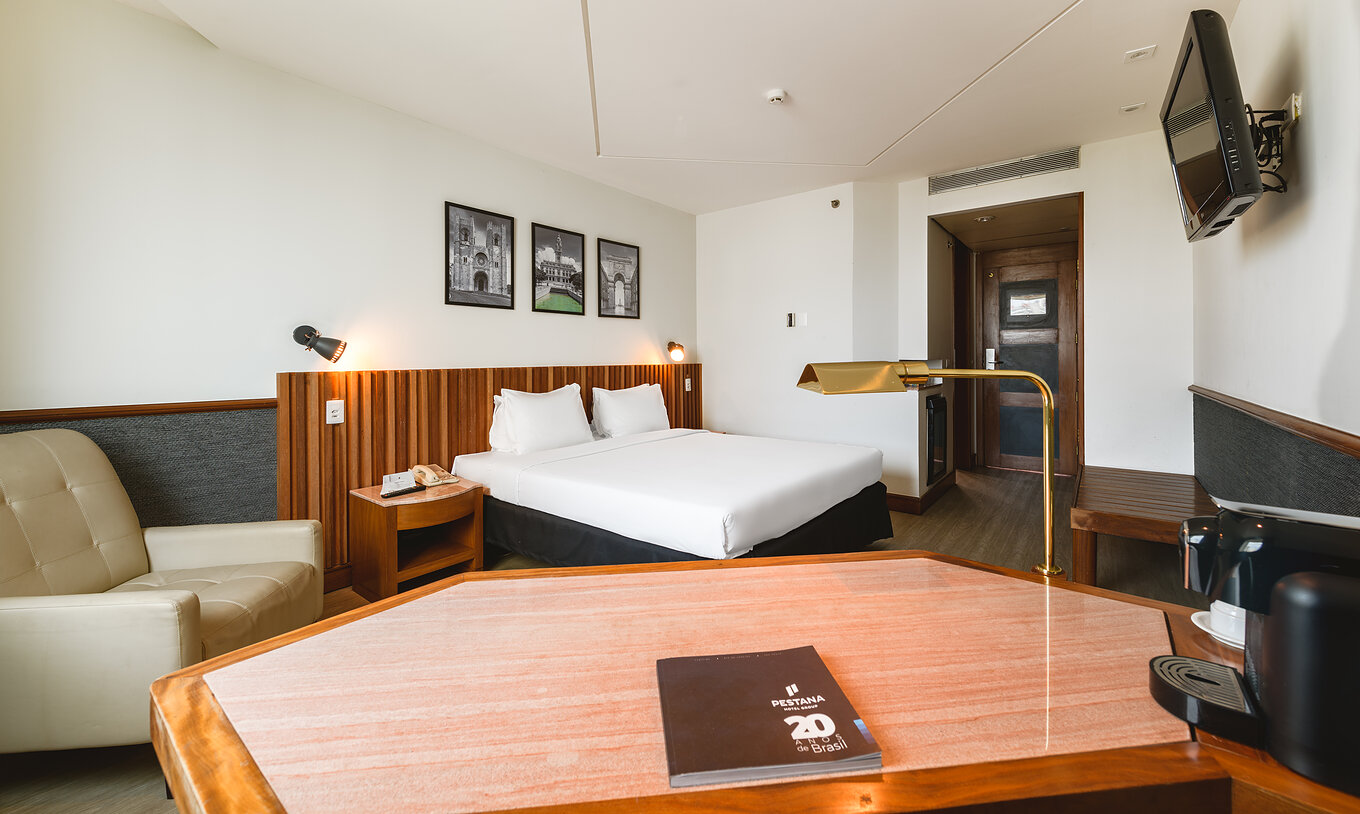 De Deluxe van Pestana São Paulo heeft een tweepersoonsbed, televisie, fauteuil en een bureau met een gouden lamp