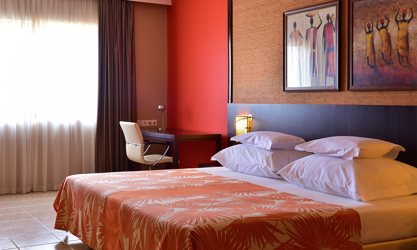 De standaardkamer van Pestana Tropico heeft een tweepersoonsbed, bureau met stoel en nachtkastje met lamp