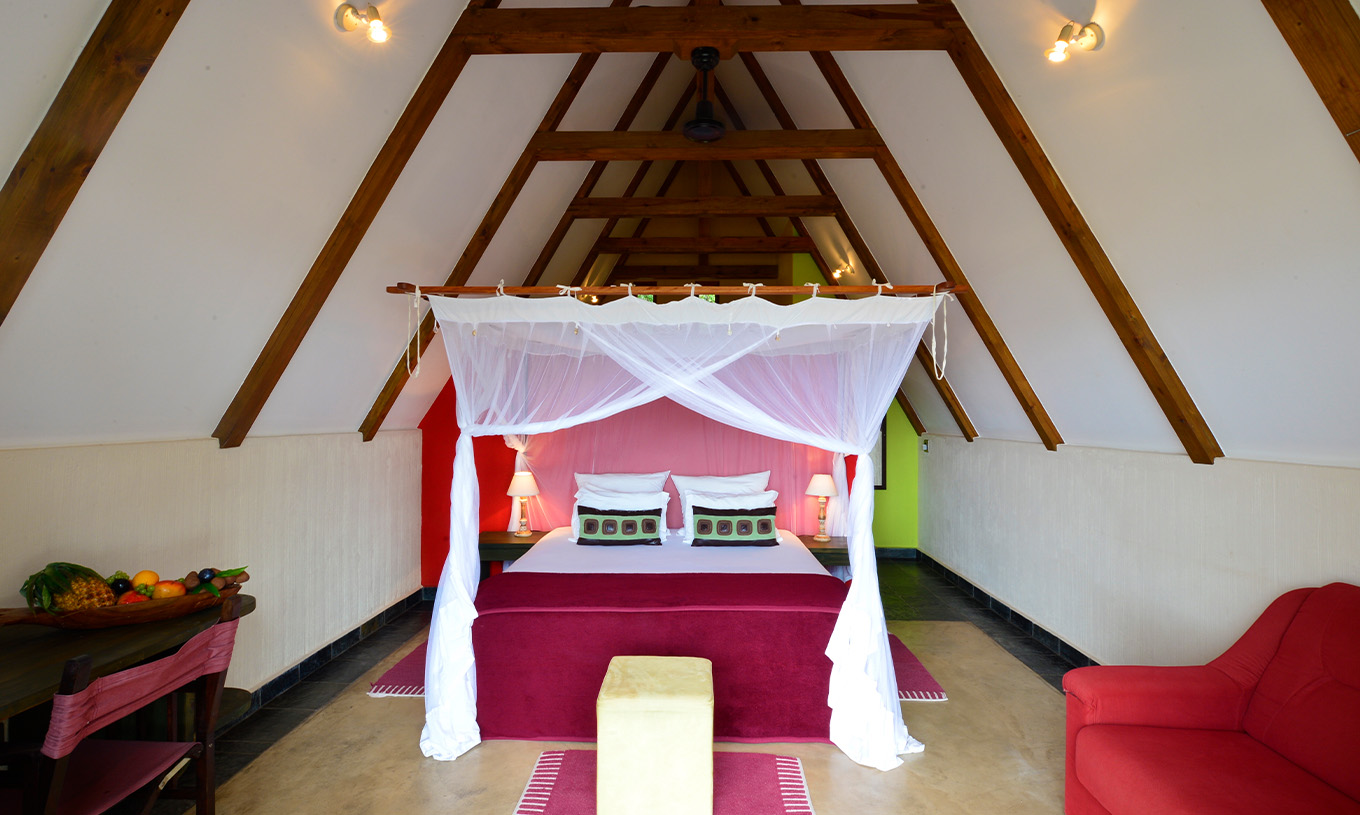 Bungalow T1 van Pestana Bazaruto Lodge heeft tweepersoonsbed met hemelbed, bank en bureau met fruitschaal