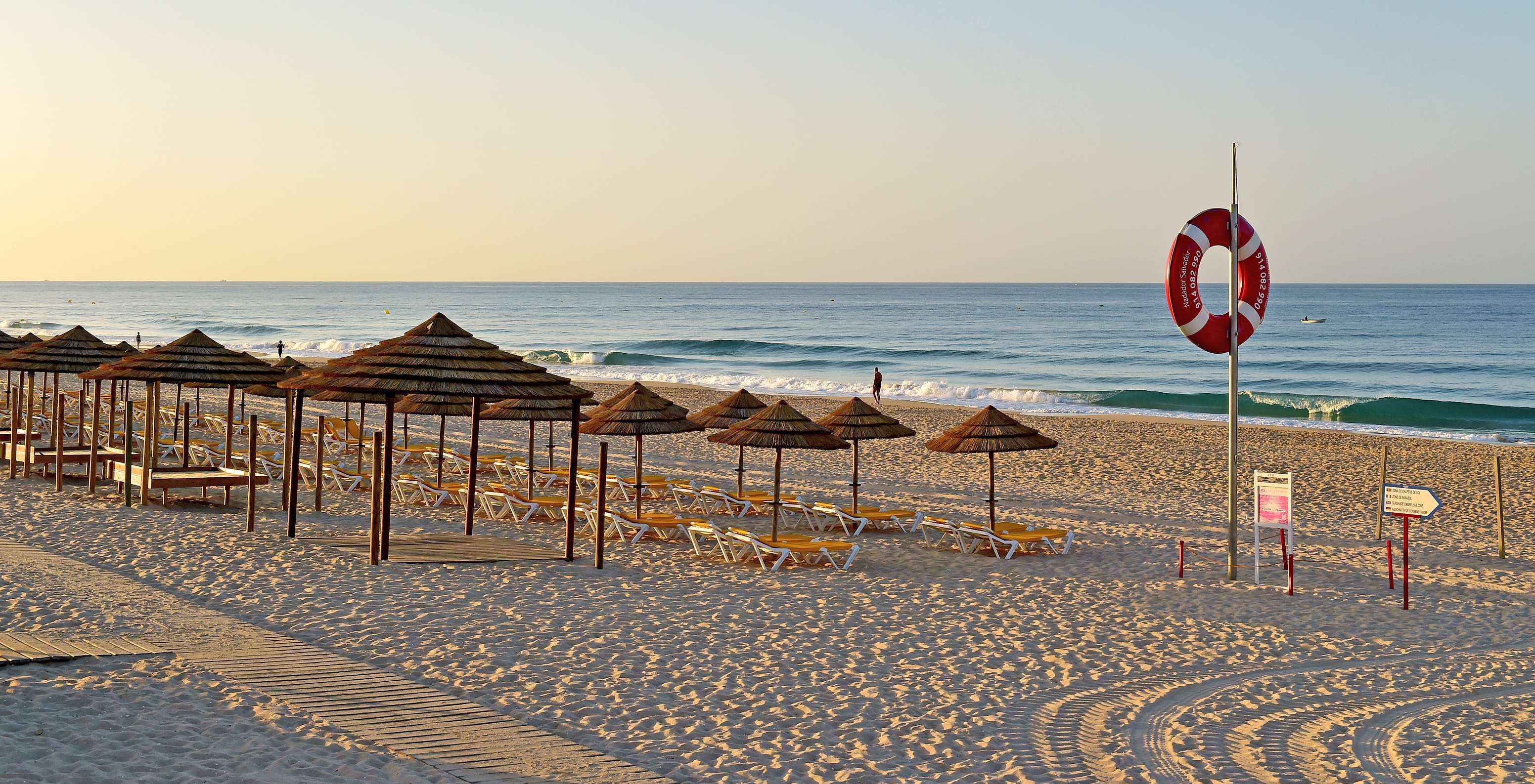 Parasols met ligbedden op het strand van Alvor, met licht zand en een rustige zee, een vredig tafereel