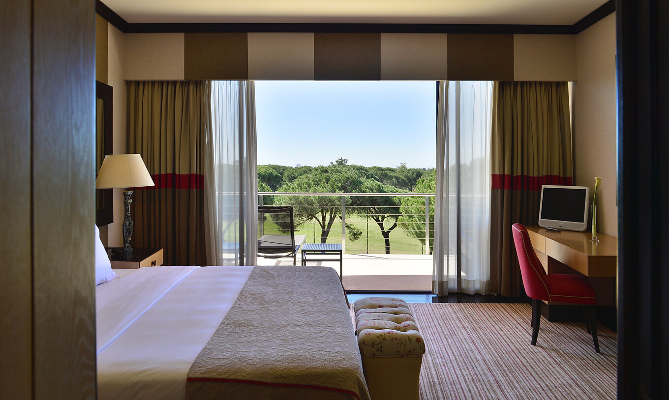 De Presidential Suite van Pestana Vila Sol - Vilamoura heeft een bed, bureau en balkon met uitzicht op de tuin