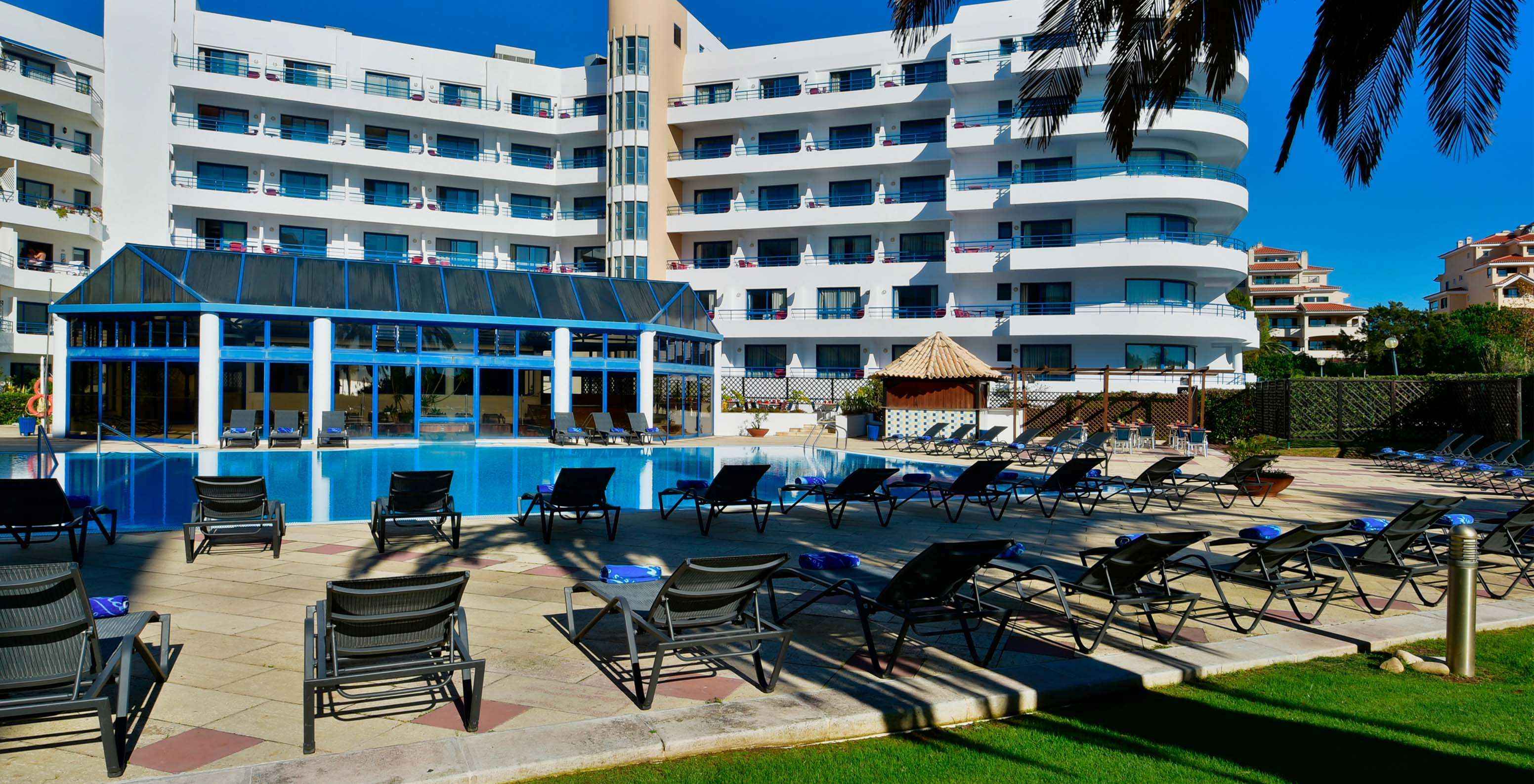 Zicht vanuit de tuin van Pestana Cascais op het buitenzwembad, ligstoelen en de zwembadbar