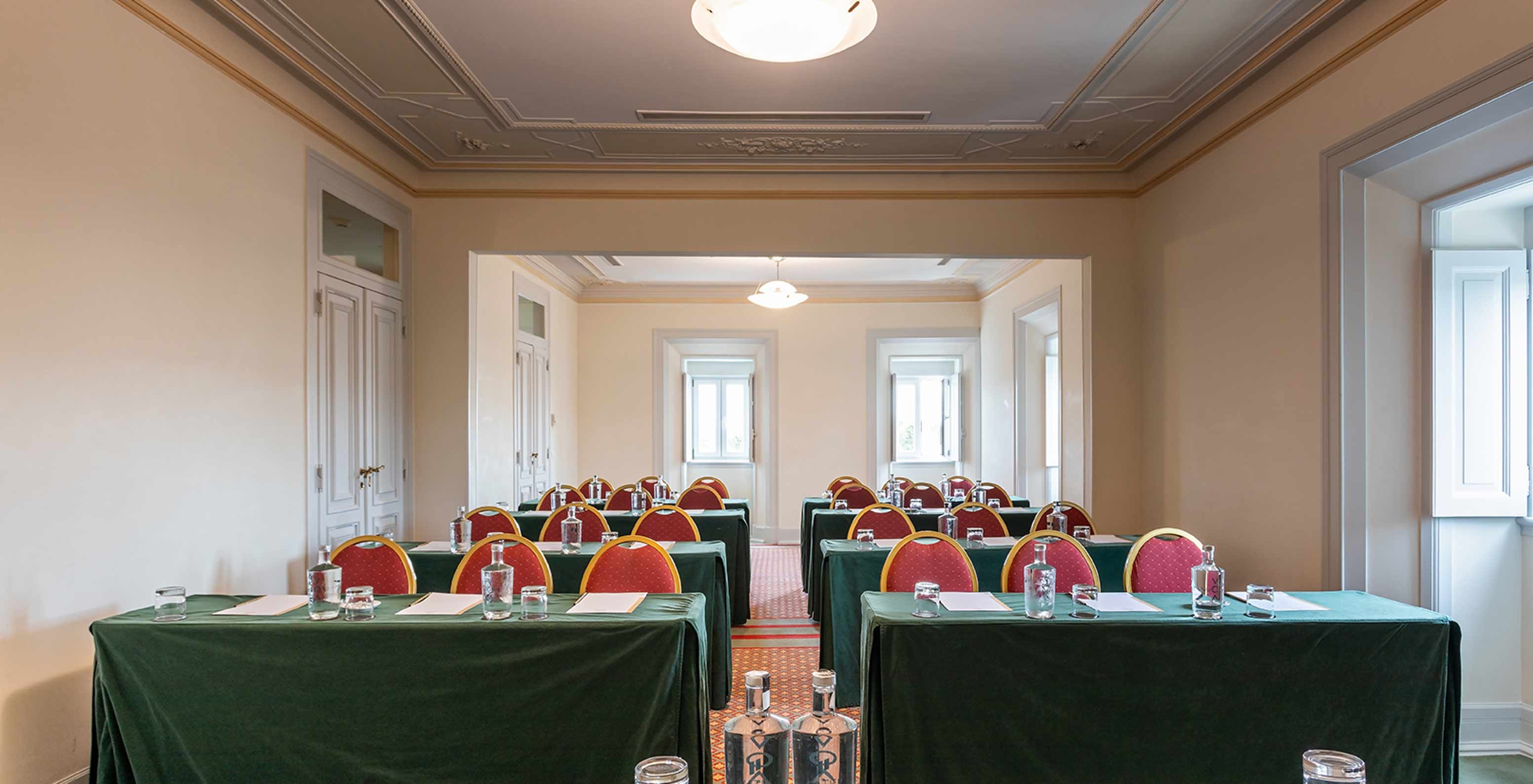 Pestana Palace Lisboa heeft een lichte vergaderzaal met meerdere groene tafels en rode stoelen	