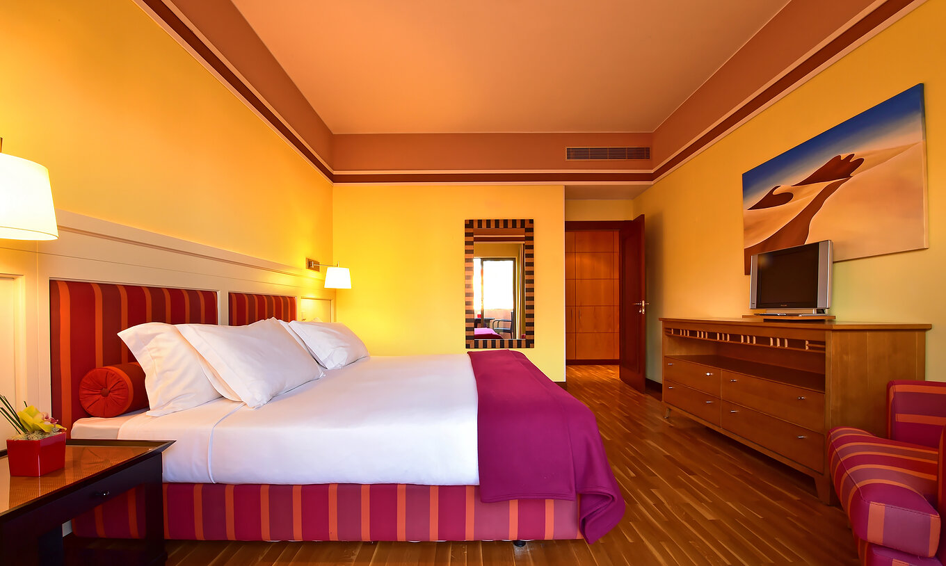 De Superior Suite van Pestana Sintra Golf heeft een tweepersoonsbed, spiegel aan de muur en meubel met televisie