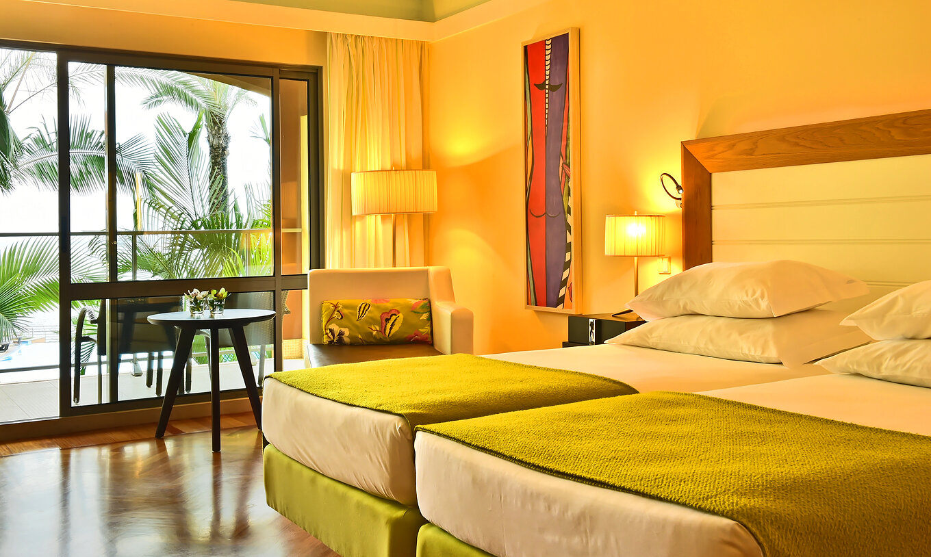 De Vista Zwembad Kamer van Pestana Promenade heeft twee bedden met een groene dekbed en een groot raam naar het balkon