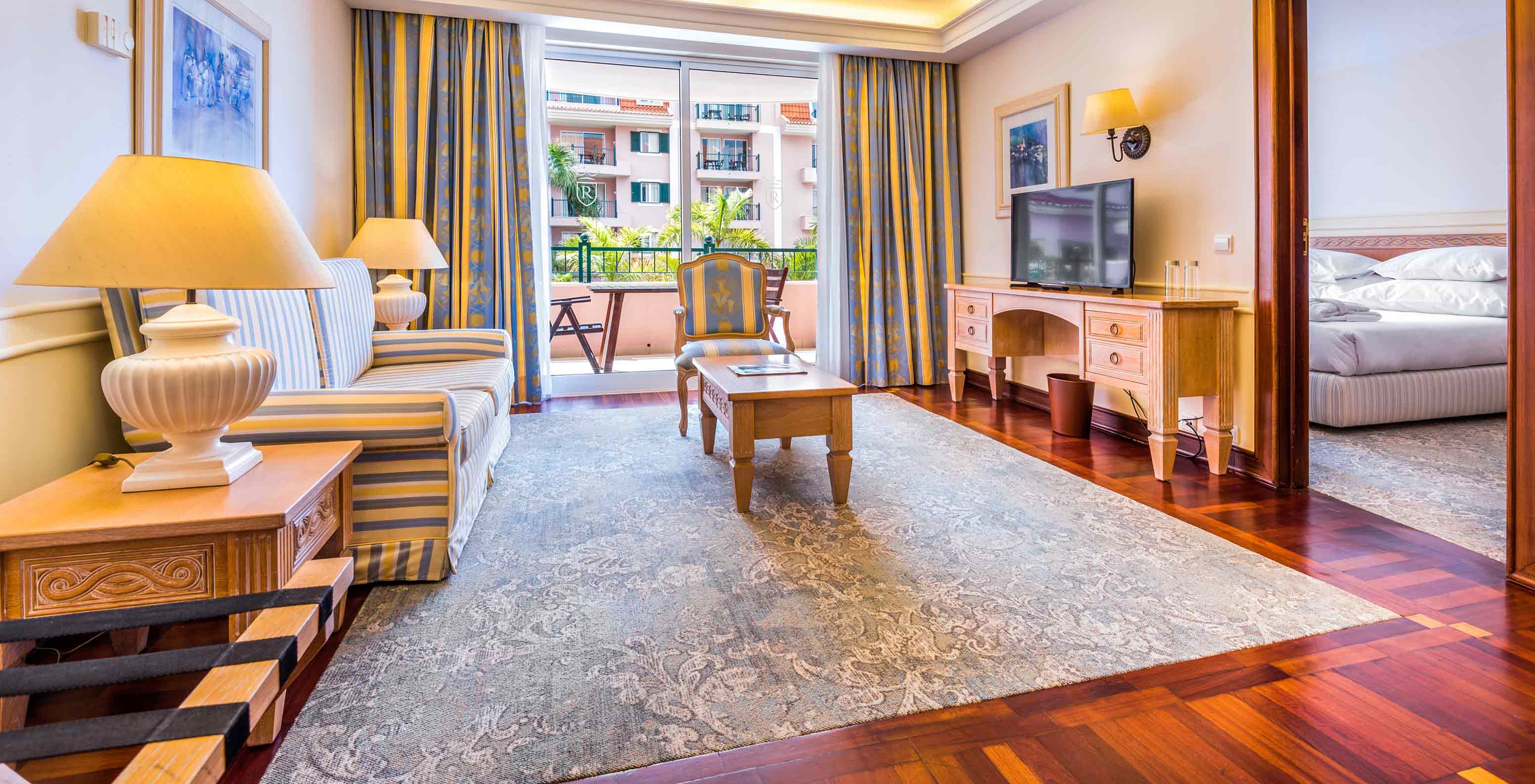 De suite van het Pestana Royal All Inclusive heeft een woonkamer met een tv, stoelen en een balkon.