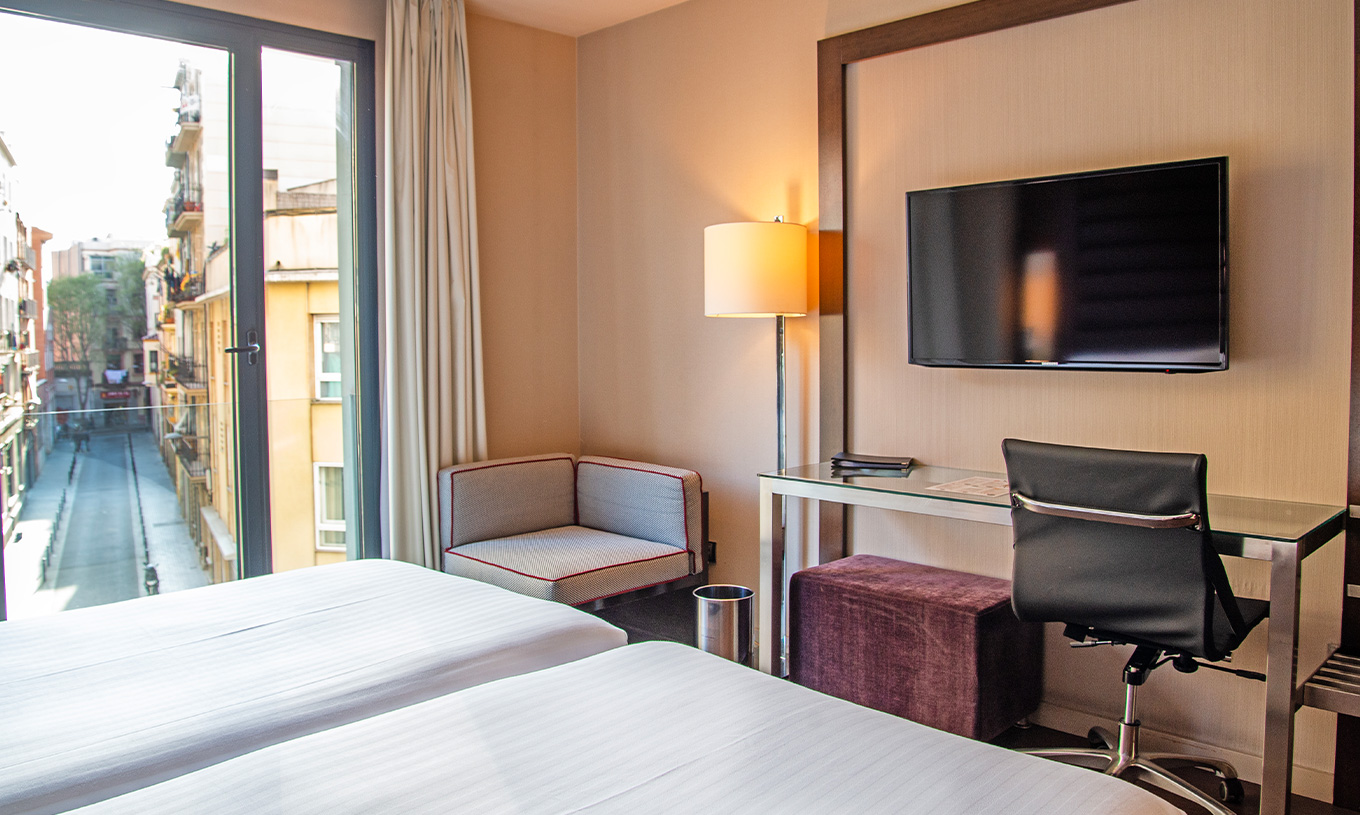Standard kamer van Pestana Arena Barcelona heeft bureau, televisie en raam met uitzicht op stad