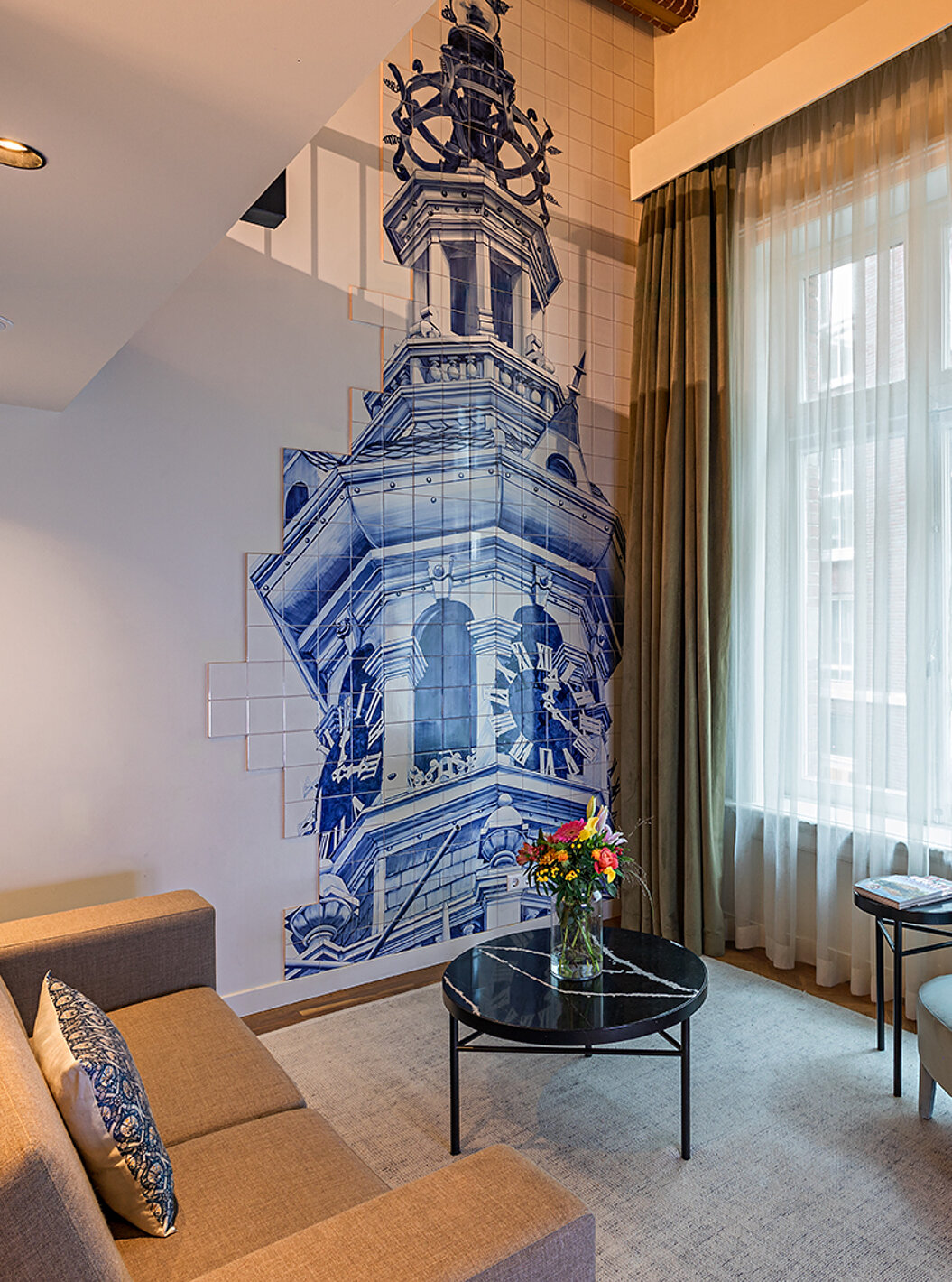 Suite Mezzanine van Pestana Amsterdam Riverside heeft woonkamer met bank, salontafel met bloemen en tegels