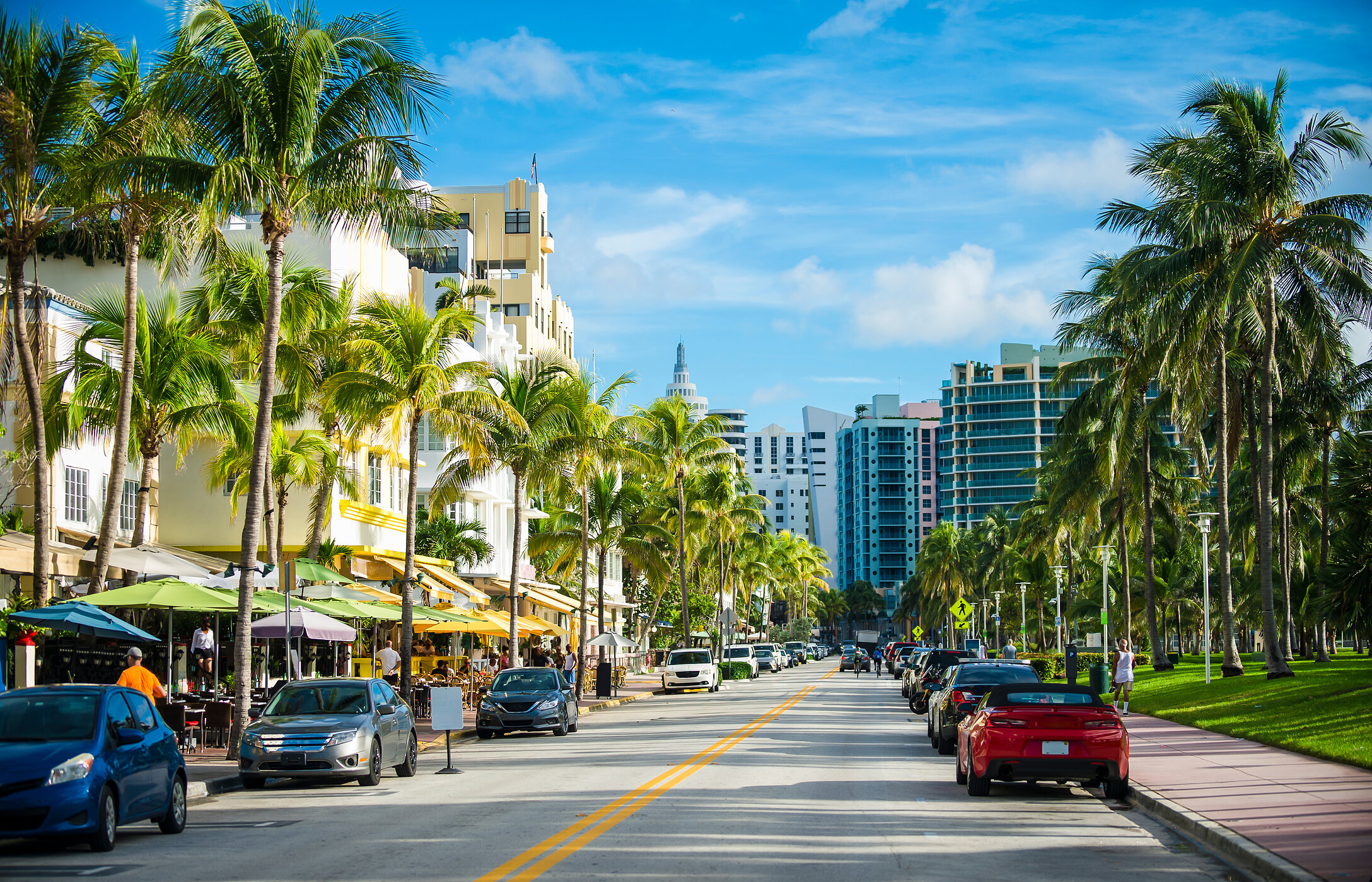 Uitzicht op Ocean Drive in Miami, met hoge palmbomen, Art Deco-gebouwen en verschillende geparkeerde auto's