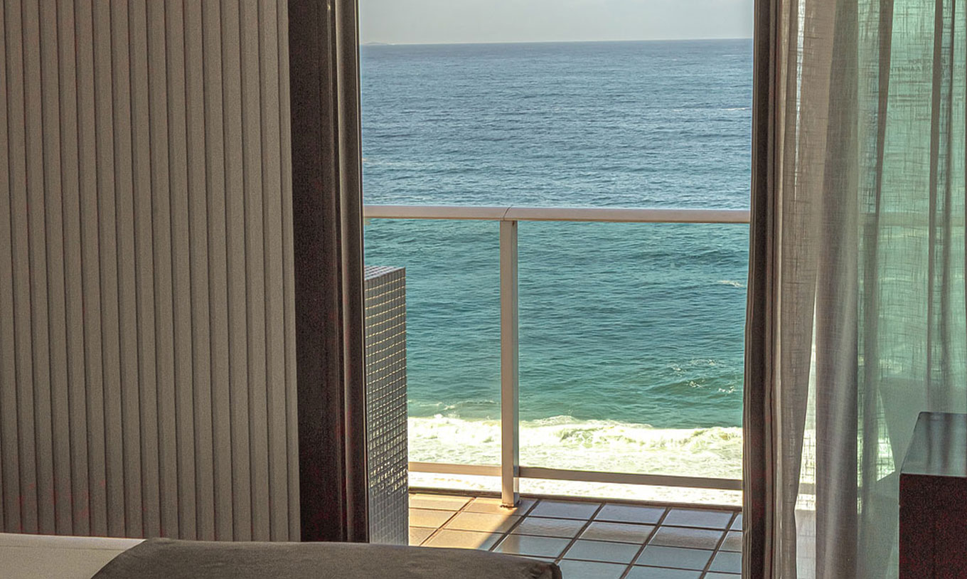 A Suite Oceânica do Pestana Rio Atlântica tem uma varanda com cortinas abertas e vista para o mar a partir do quarto