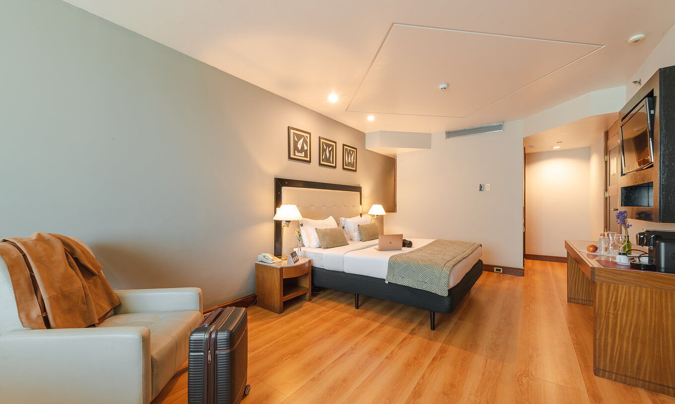 A Suite Executiva do Pestana São Paulo tem um quarto com cama de casal, poltrona e uma mala de viagem