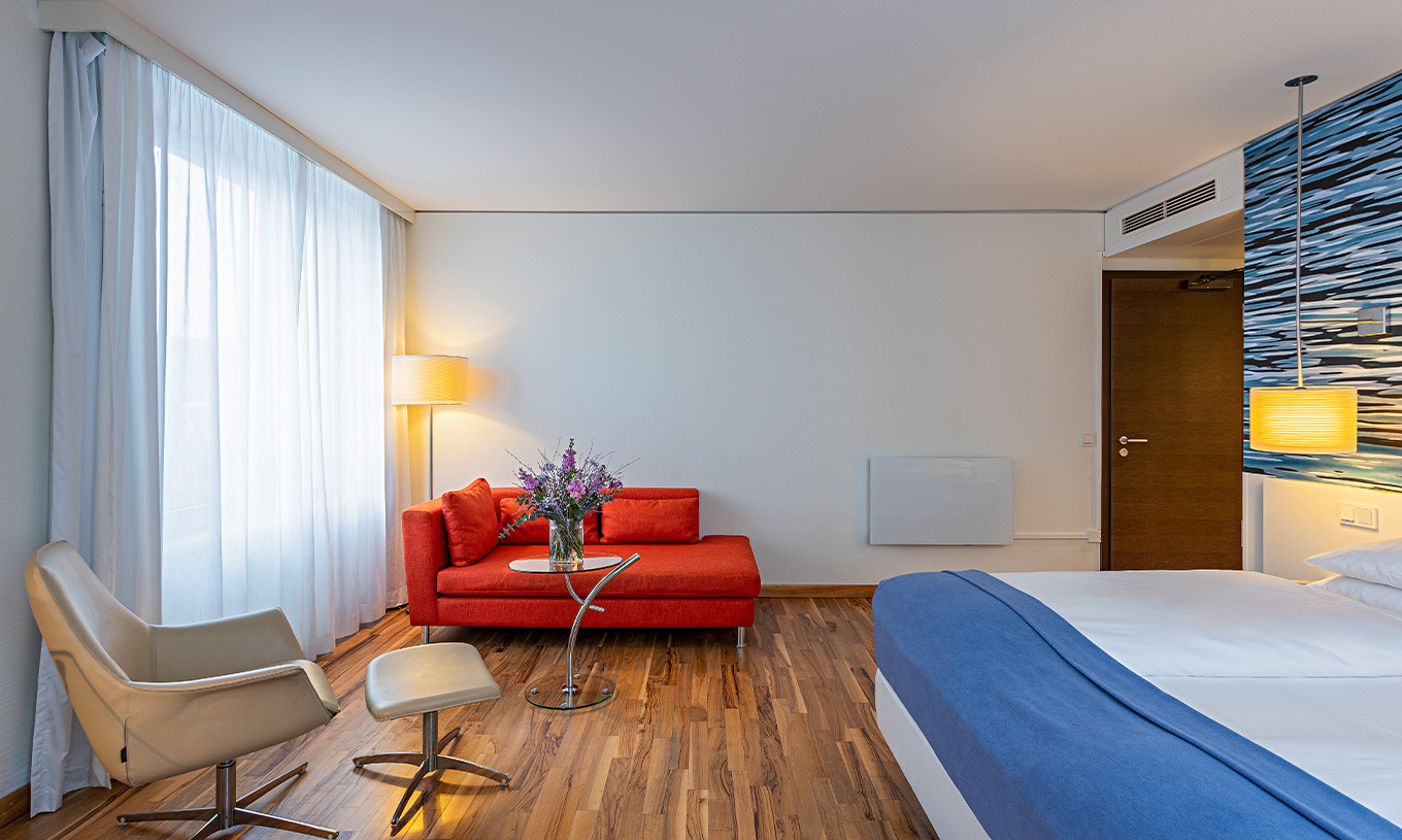 O quarto Grand Deluxe do Pestana Berlin Tiergarten conta com uma cama de casal, um sofá, mesa de centro, e um cadeirão