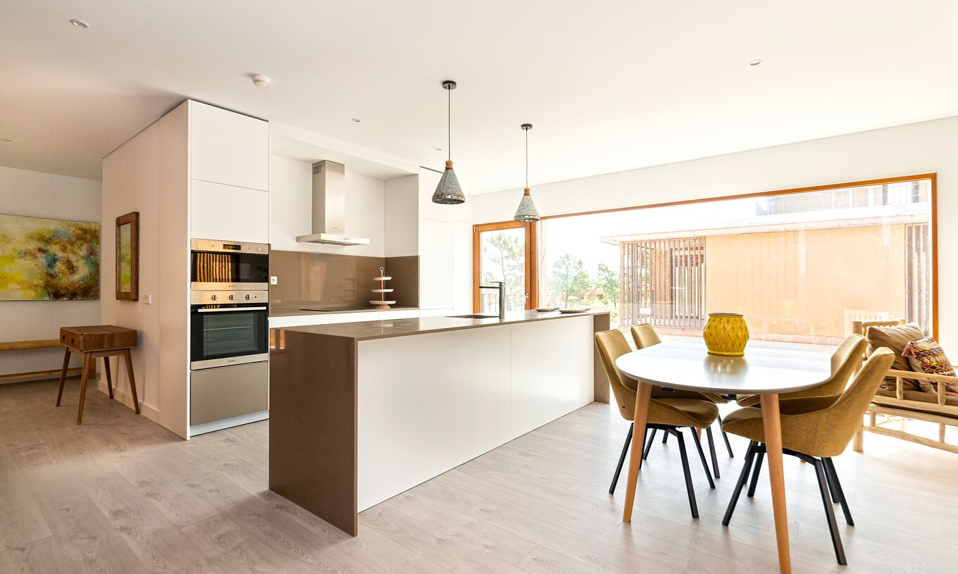 Apartamento Eco Village 1º Andar Vistas com Piscina no Pestana Tróia, exibindo cozinha moderna integrada com sala de jantar iluminada por ampla janela de vidro