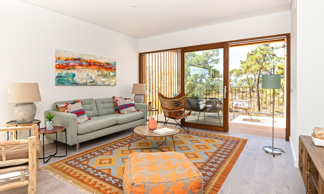 Apartamento Eco Village 1º Andar Vistas com Piscina do Pestana Tróia exibindo sala de estar iluminada com sofá cinza, tapete colorido e varanda com vista para árvores