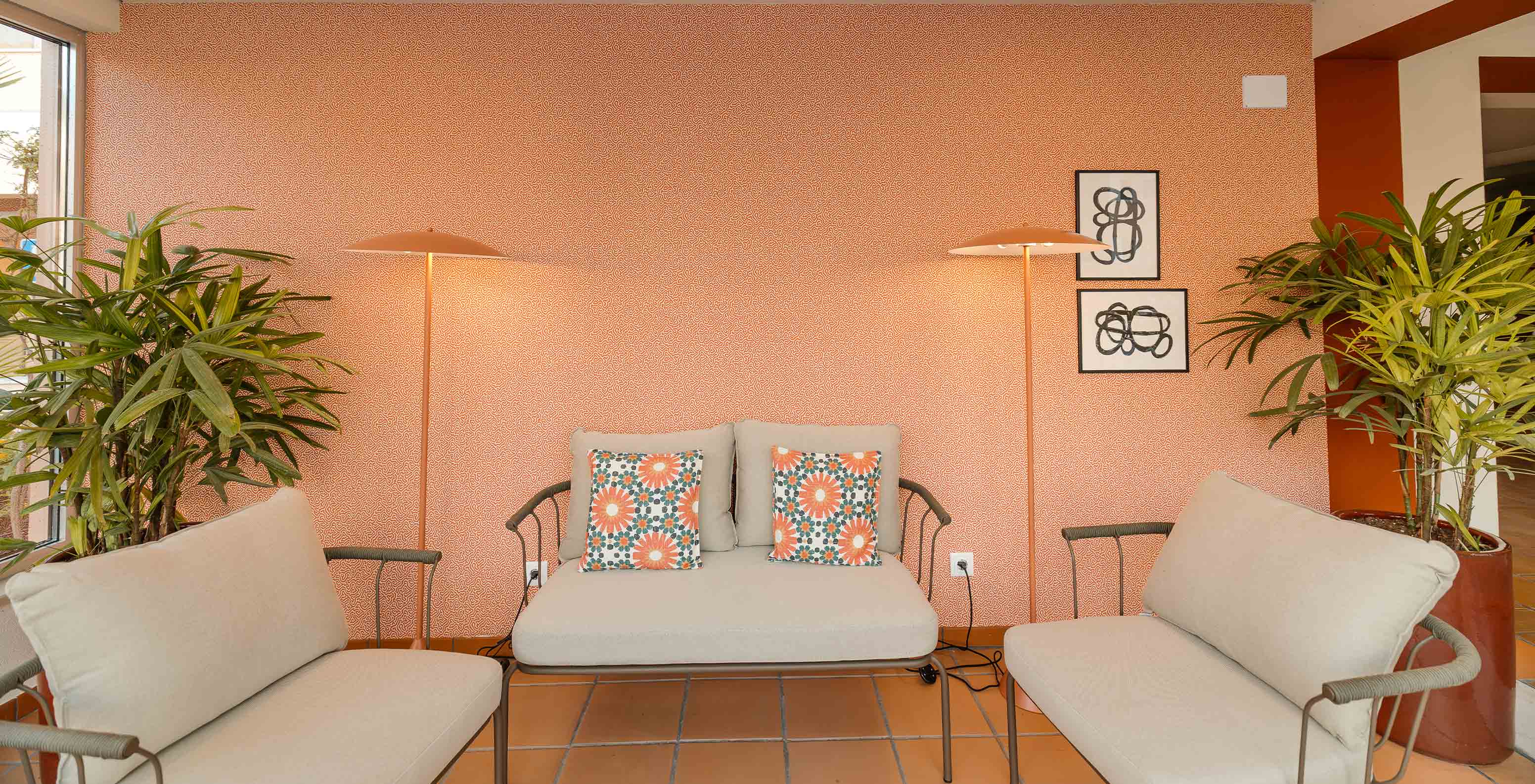 Hall do Hotel Perto da Praia com Piscina, com papel de parede laranja e três sofás confortáveis em tom bege