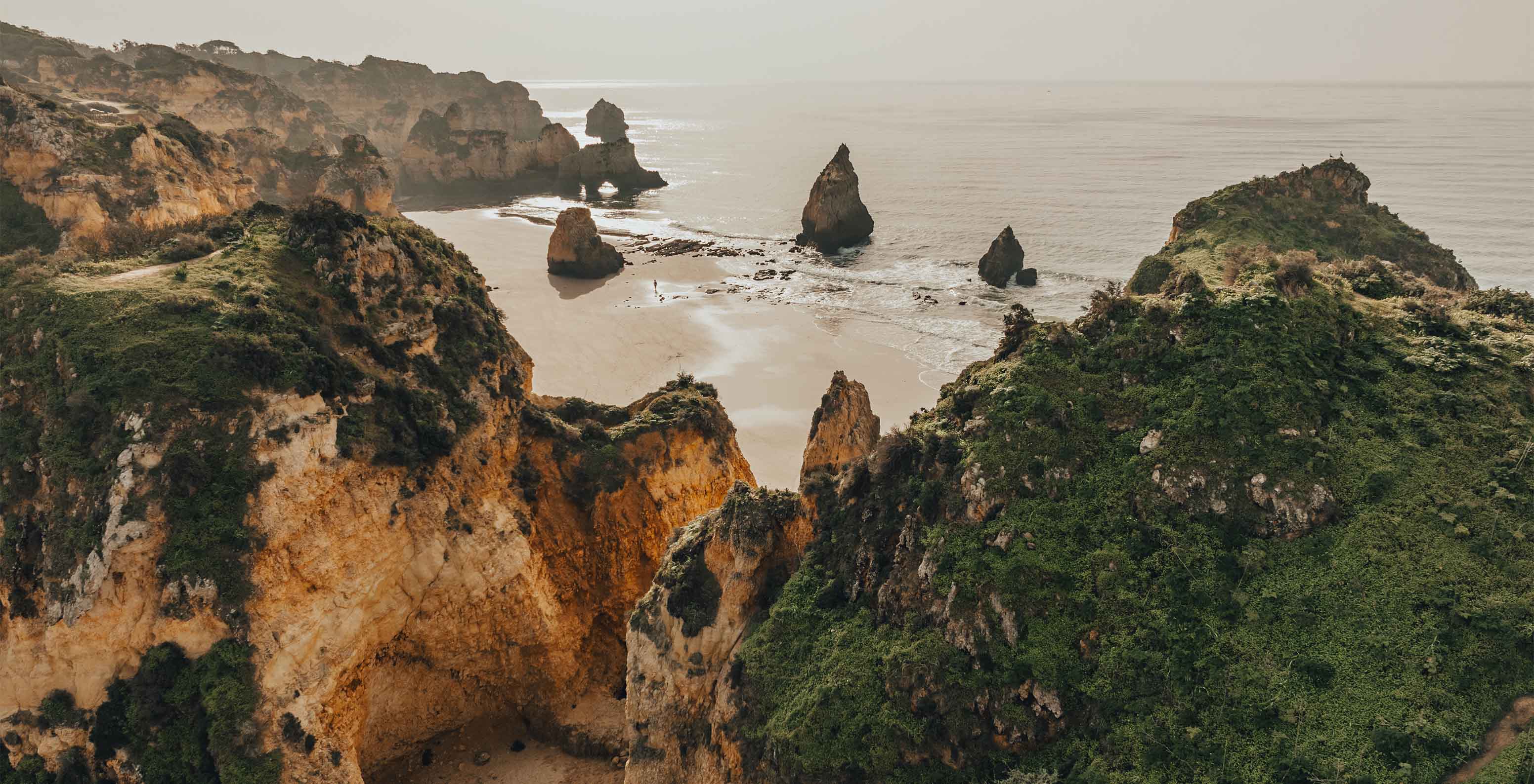 Vista de cima da Praia dos Três Irmãos, com as formações rochosas e vegetação, em direção ao mar com nevoeiro