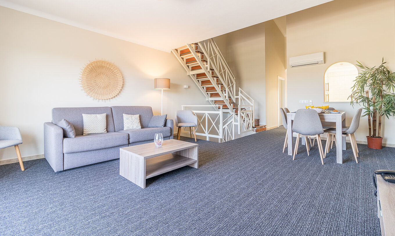 O Apartamento T2 do Pestana Gramacho Residences tem uma sala de estar com um sofá cinzento, mesa de centro e escadas ao fundo