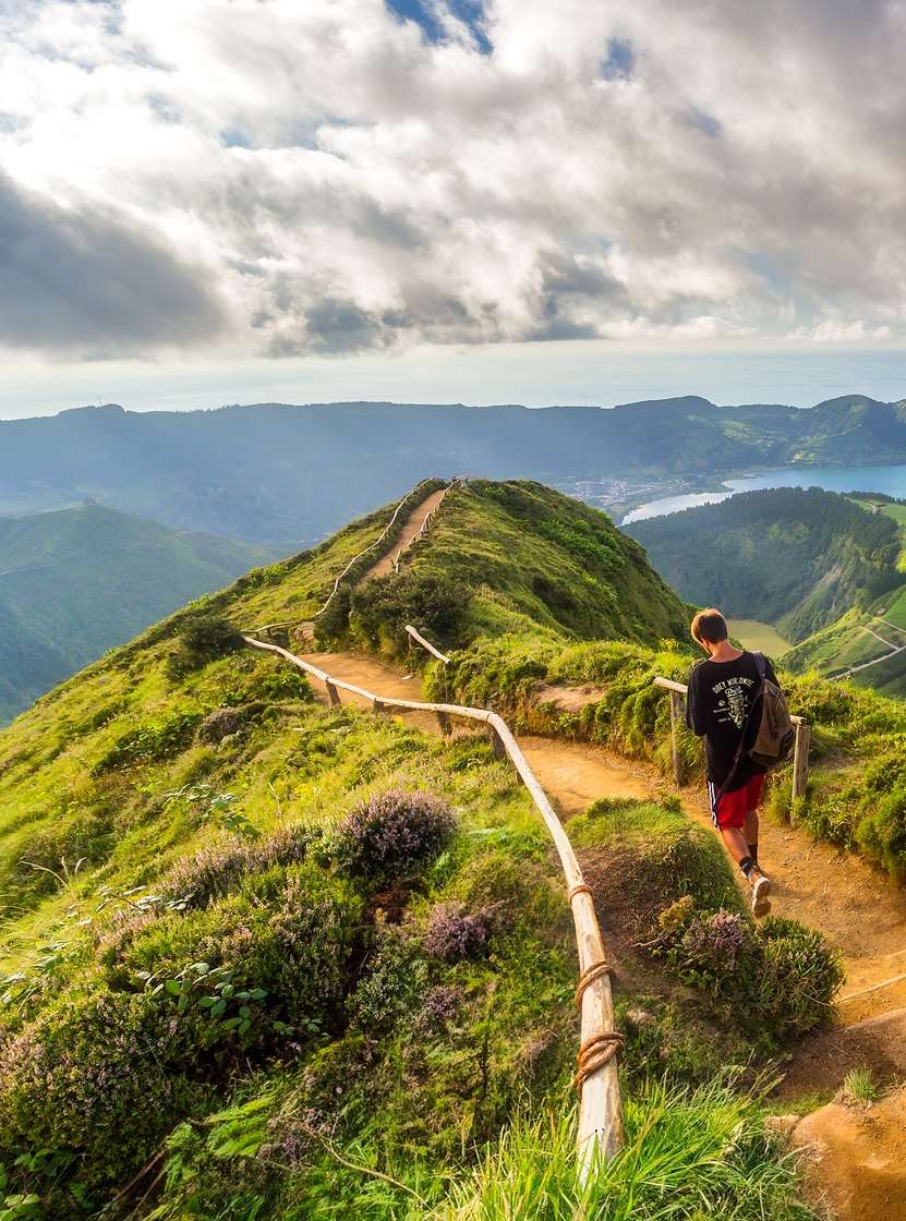 Homem caminha num trilho de terra com vista para a Lagoa das Sete Cidades, na Ilha de São Miguel, nos Açores