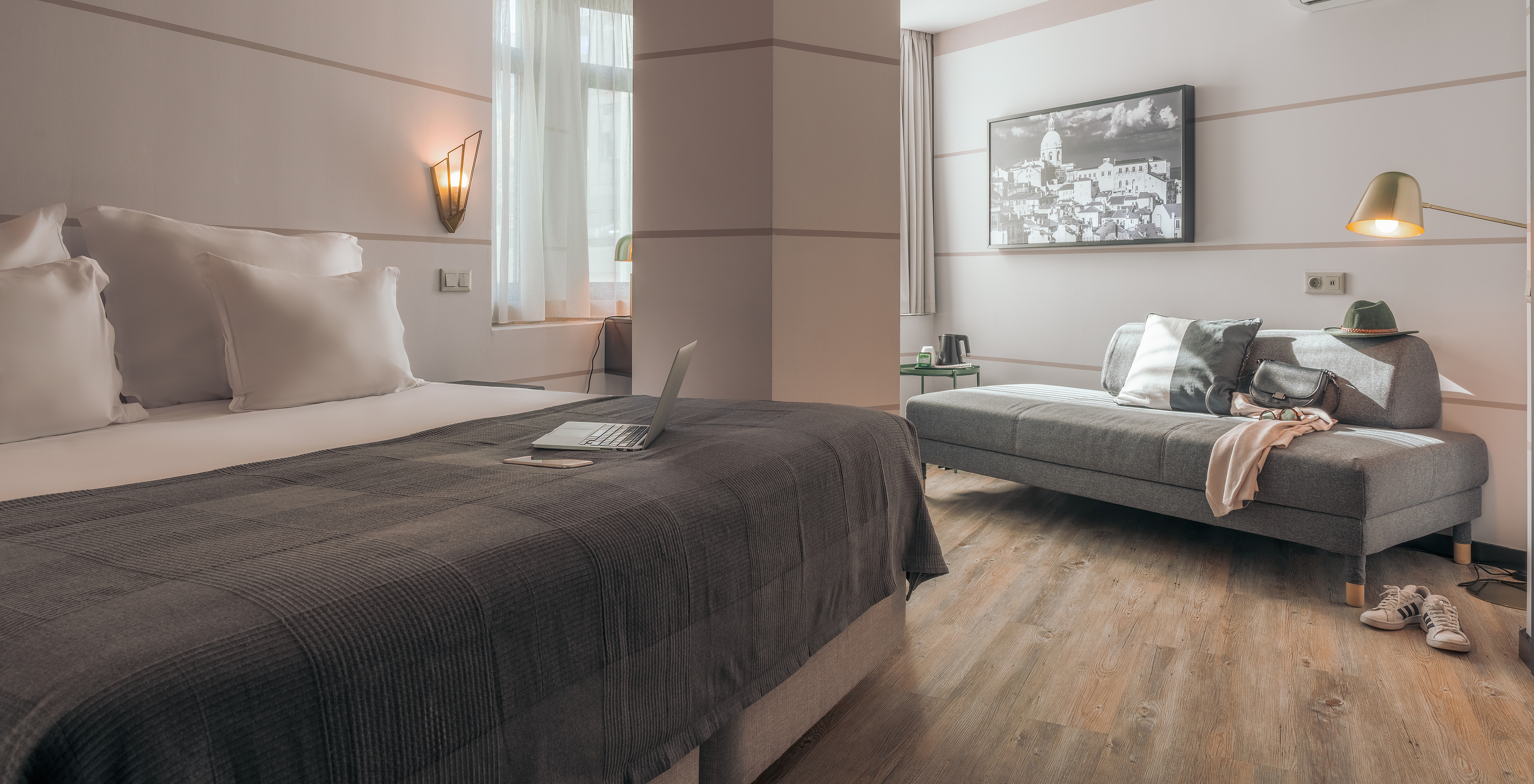 O Double Superior do Pestana Lisboa Vintage tem uma cama de casal com manta cinzenta, um sofá cinzento e uns ténis brancos
