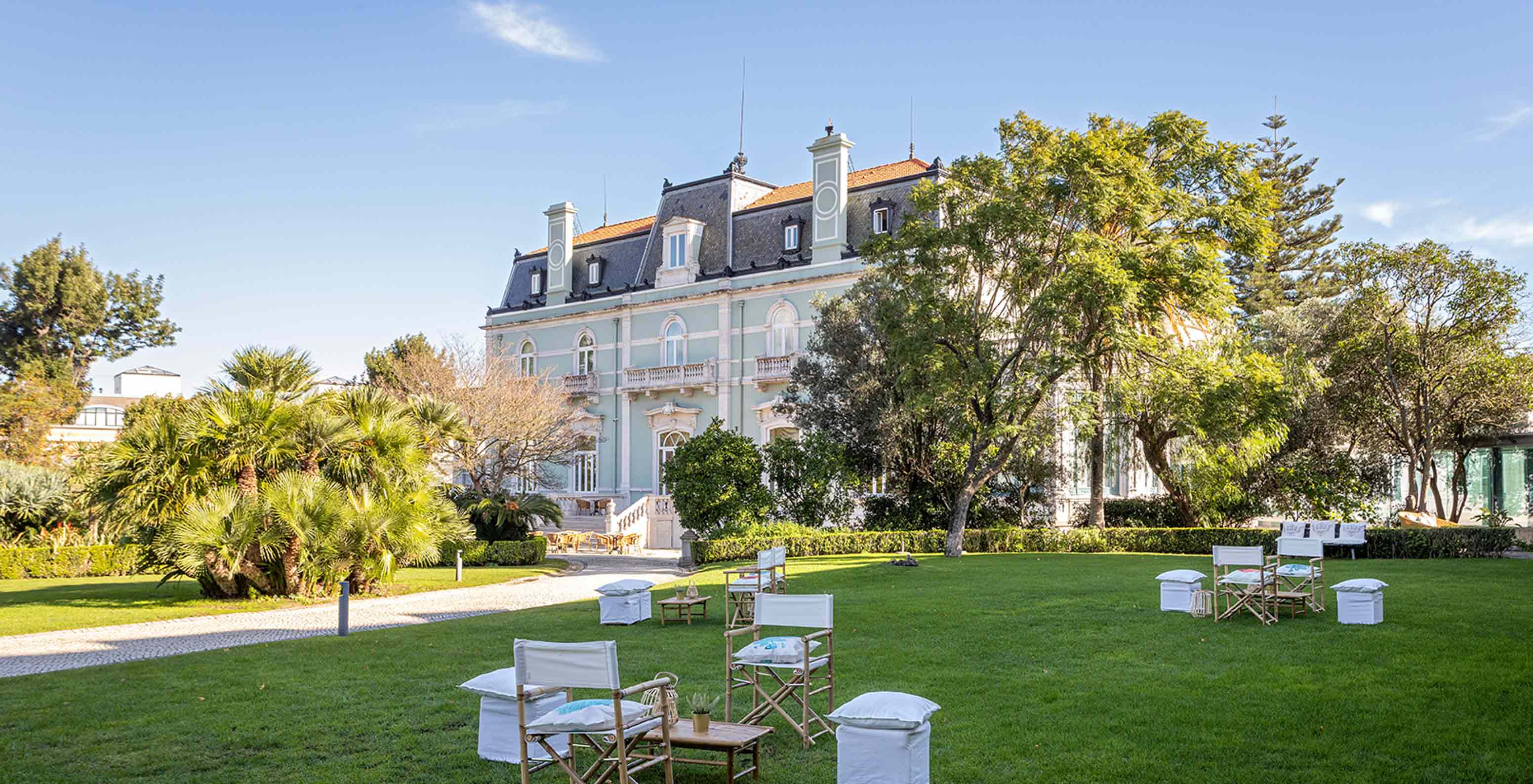 O Pestana Palace Lisboa tem um jardim com mesas e cadeiras sobre relva verde, próximo ao edifício principal