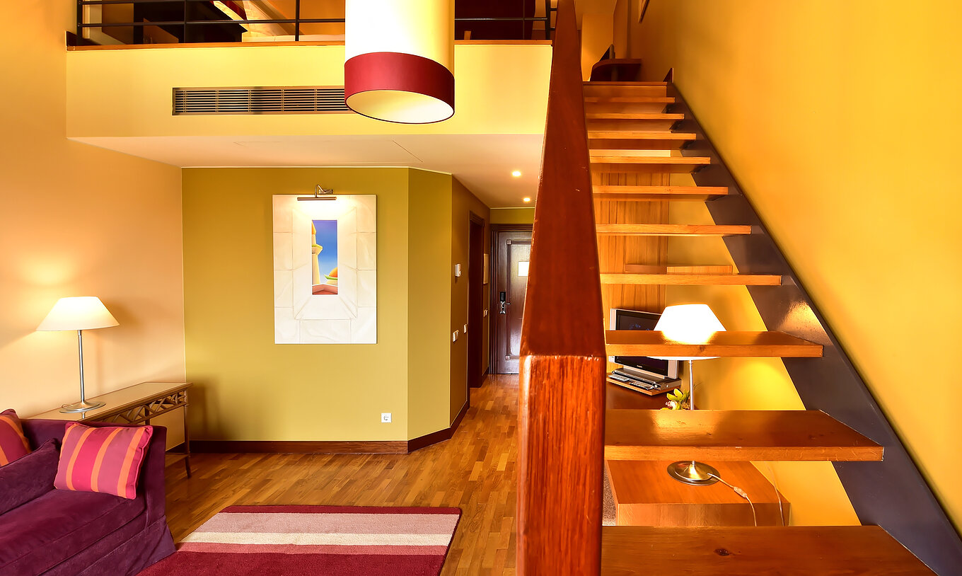 A Suite Mezzanine Jacuzzi do Pestana Sintra Golf tem um sofá, umas escadas para a mezzanine, uma quadro e um candeeiro