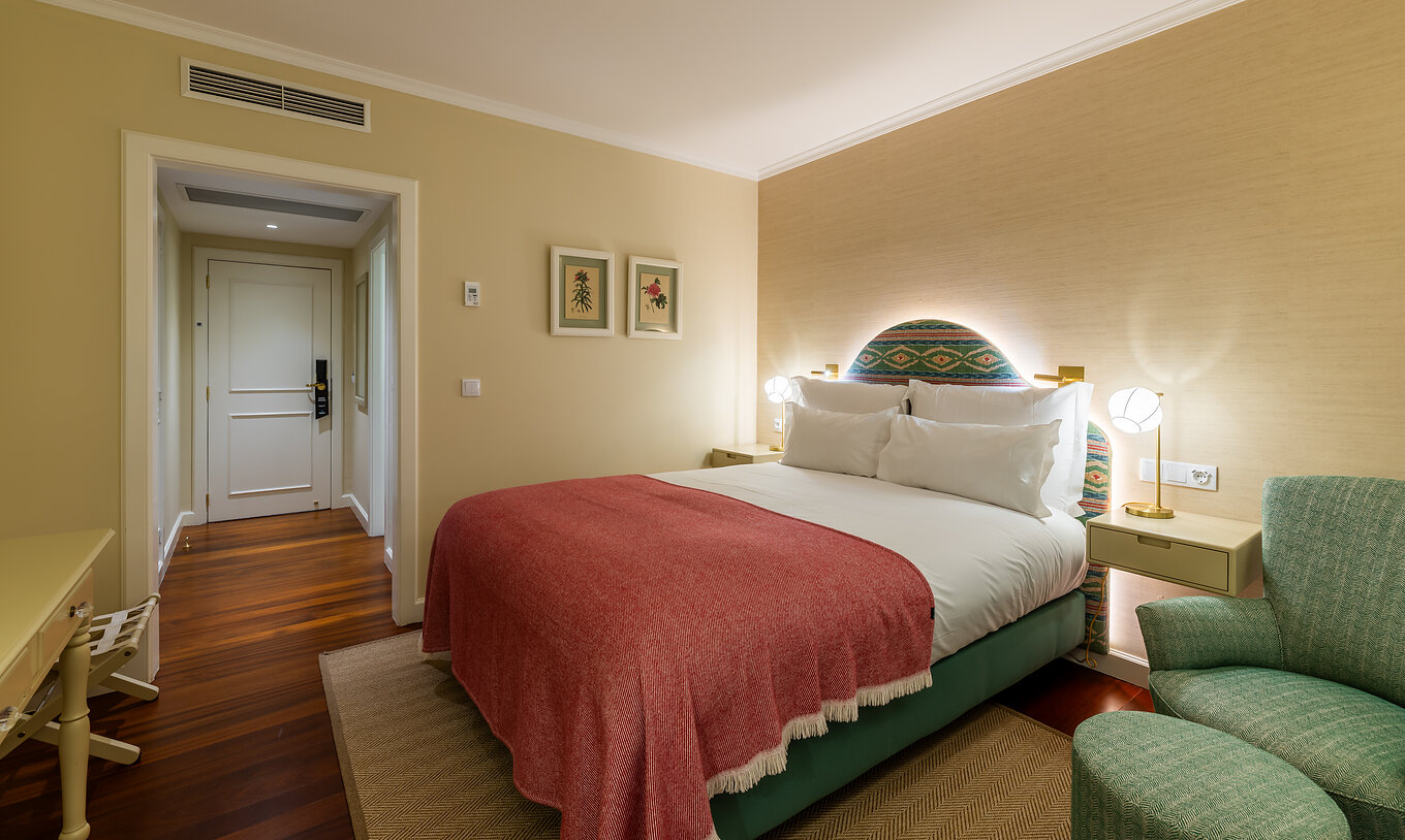 O Quarto Vista Mar Parcial do Pestana Quinta Perestrello tem uma cama de casal com uma colcha rosa e uma poltrona verde