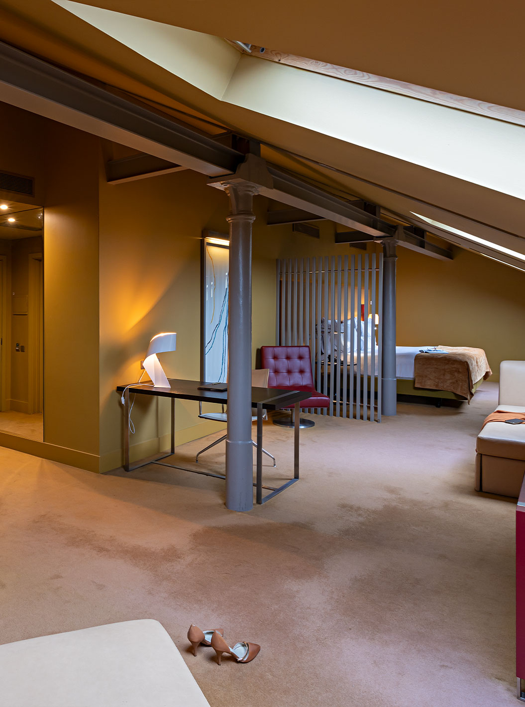 O Loft Ático do Pestana Palácio do Freixo tem um sofá beje em pele, uma secretária e um móvel vermelho 