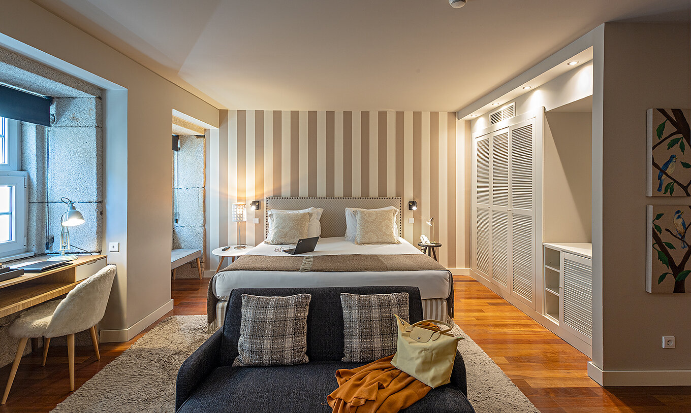 A Heritage Suite do Pestana Vintage Porto tem uma cama de casal, um sofá, uma secretária e um roupeiro branco