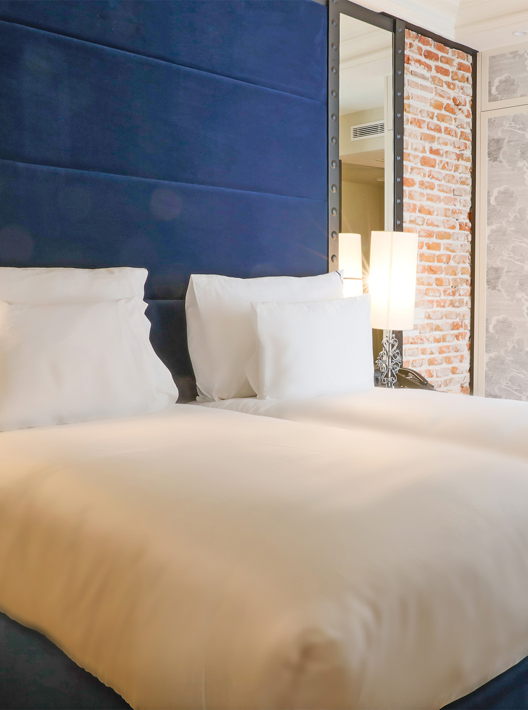 O Quarto Superior do Pestana Plaza Mayor Madrid tem duas camas com cabeceira azul e uma parede com tijolos