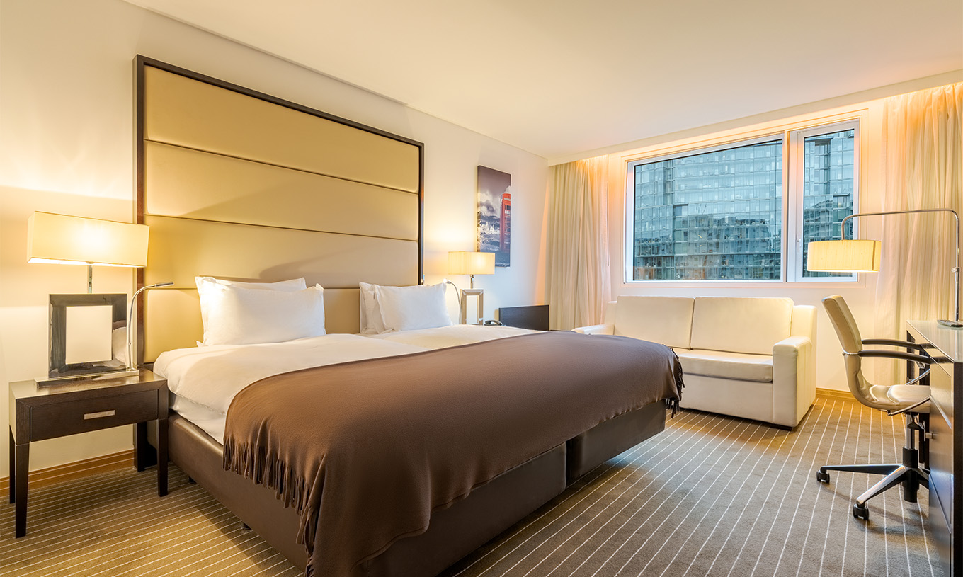 O Twin Deluxe do Pestana Chelsea Bridge tem duas camas juntas, mesa de cabeceira, sofá, candeeiros e janelas com cortinados