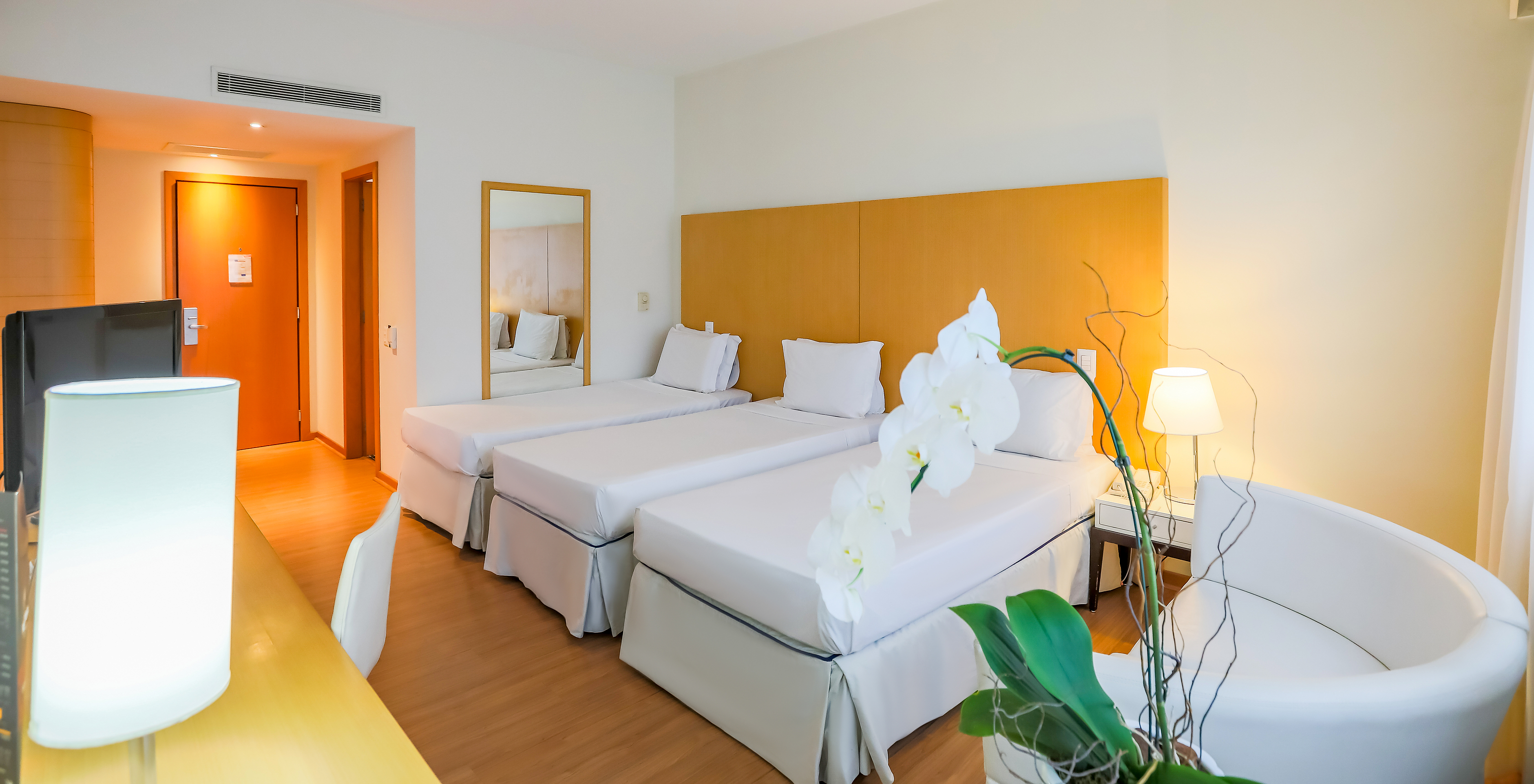 O Twin Luxo Corner do Pestana Curitiba tem três camas individuais com uma secretária com televisão e um pequeno sofá