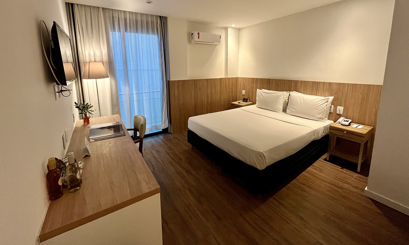 O Quarto Semi Adaptado do Pestana Rio Atlântica é um quarto com cama, secretária, TV na parede e chão em madeira