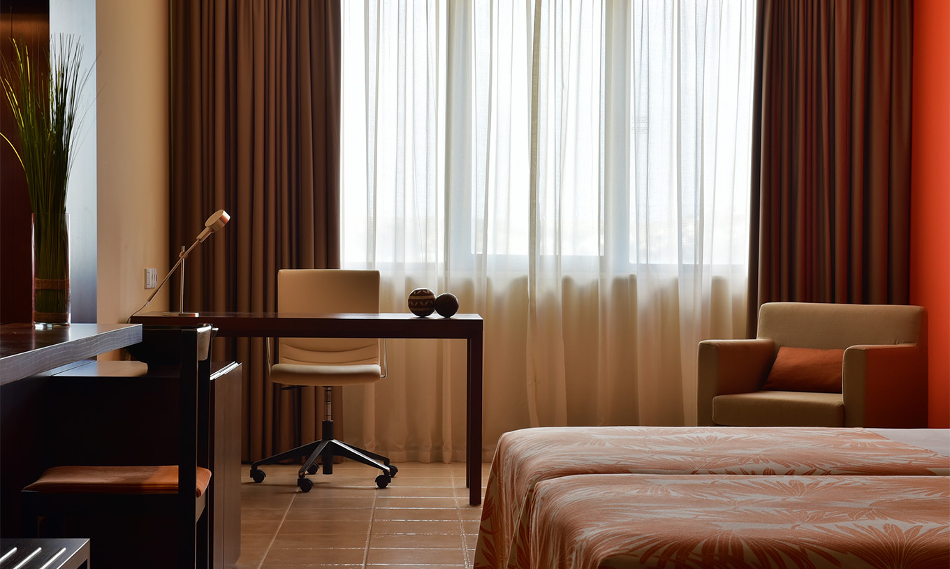 O quarto Standard do Pestana Tropico conta com uma secretária com candeeiro e uma cadeira, e um cadeirão